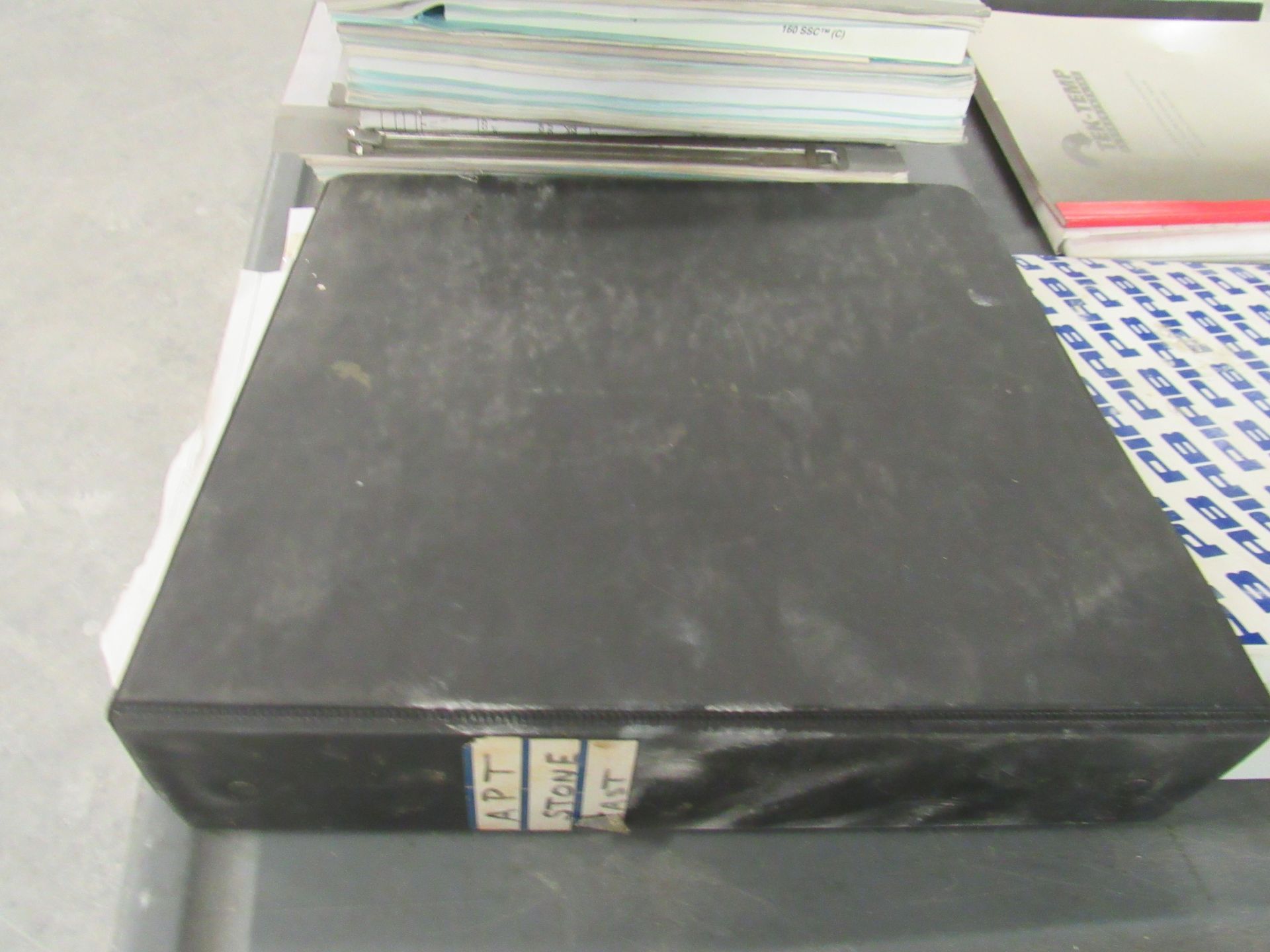 Black binder on a table with labels. Papers and other objects are also visible.
