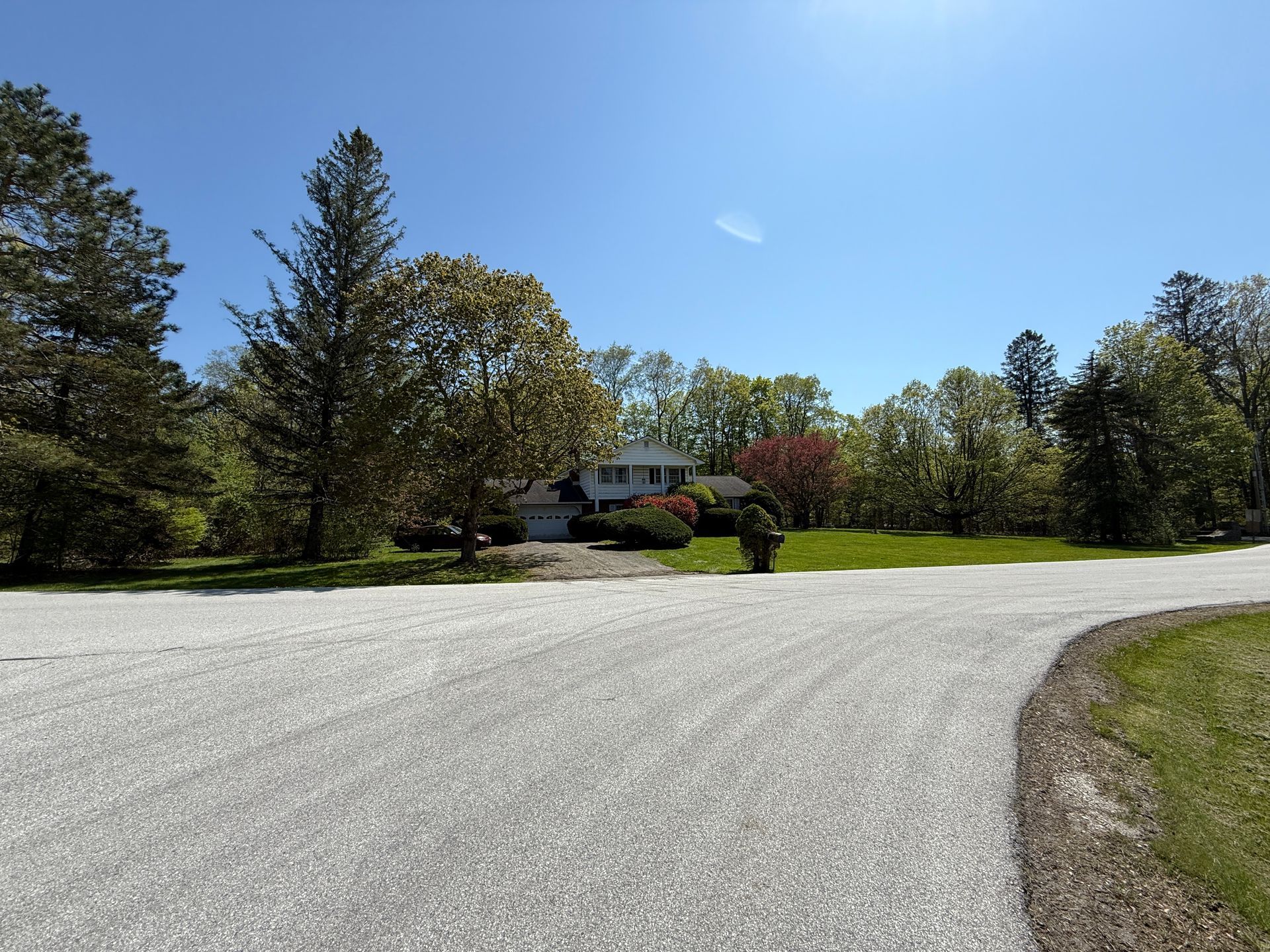 House on a sunny day with a gravel driveway. Trees surround the house, clear blue sky.