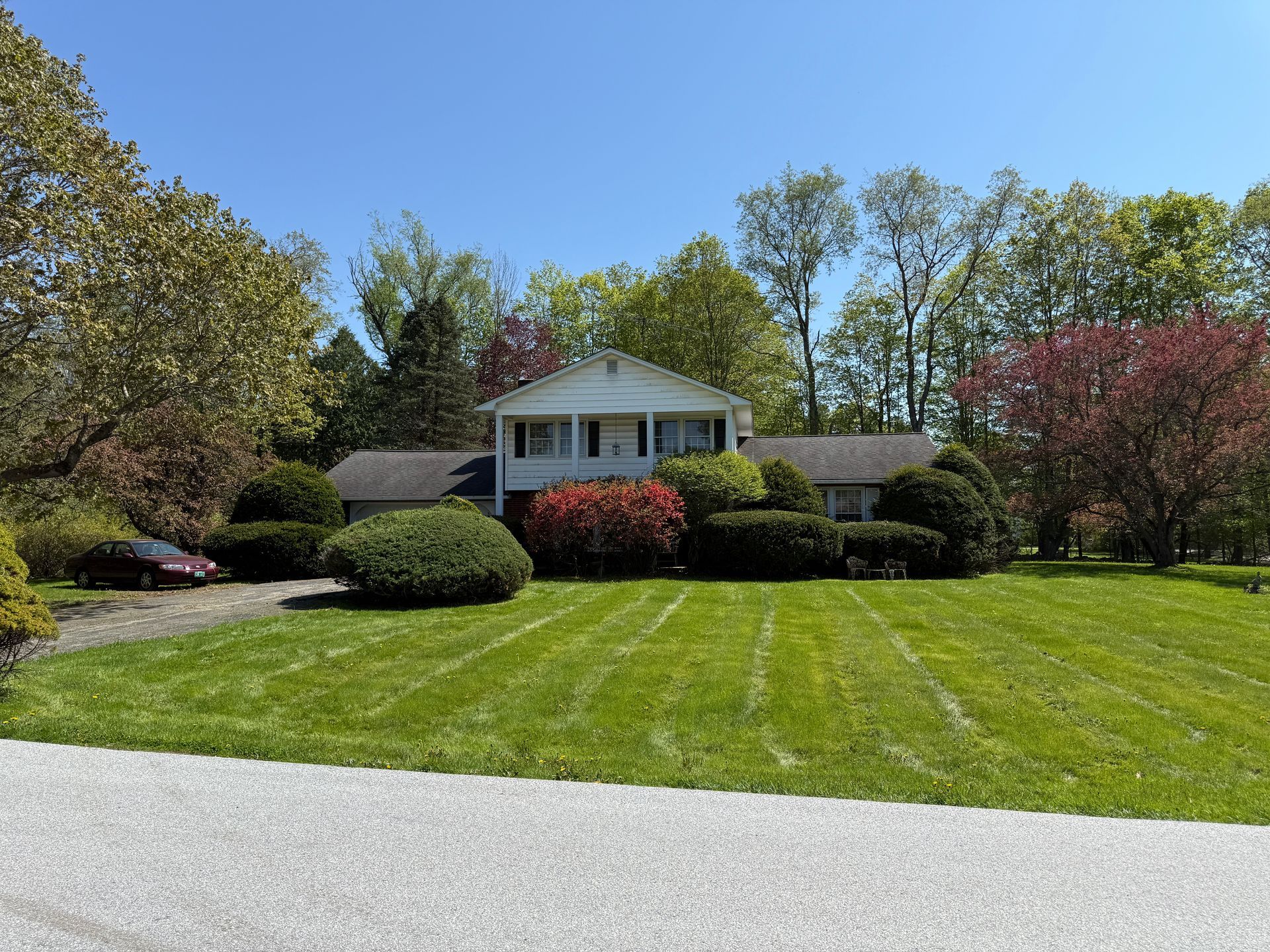 A two-story white house with green lawn, shrubs, trees, and blue sky.