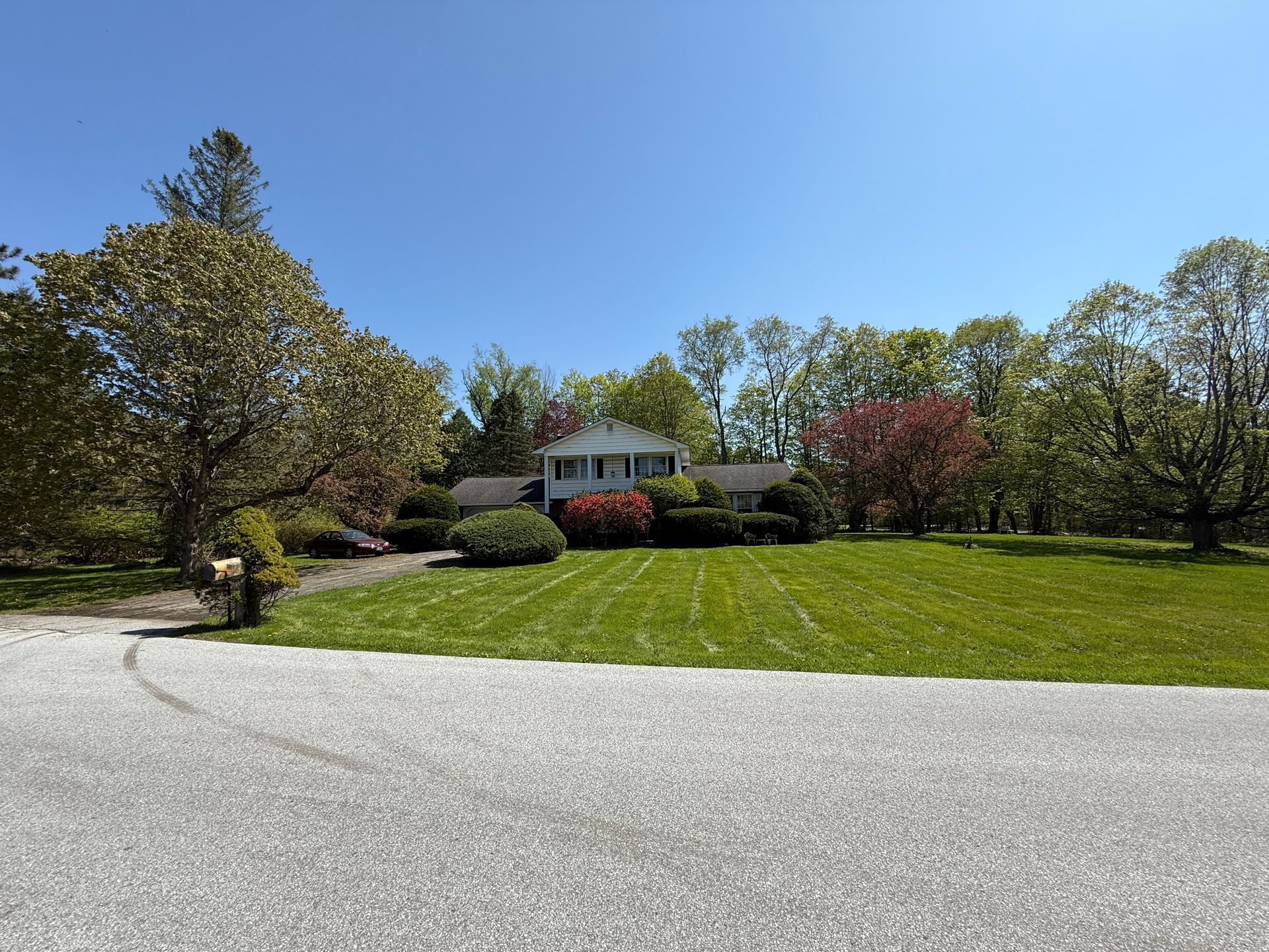 House with green lawn, trees, and blue sky in daylight.