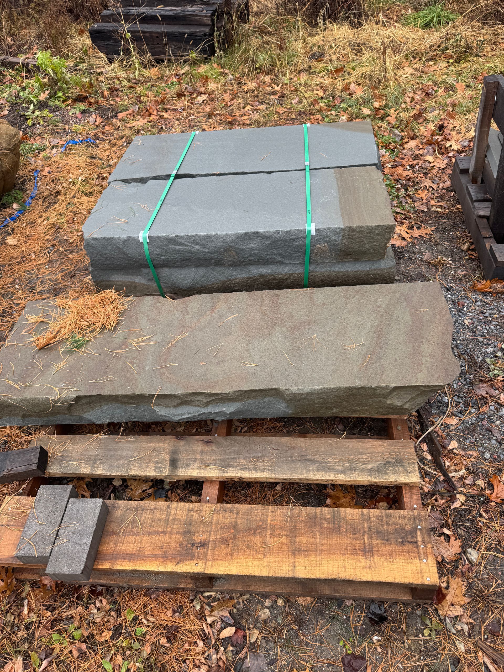 Stone slabs stacked on a wooden pallet, held together by green strapping. Outdoor setting.