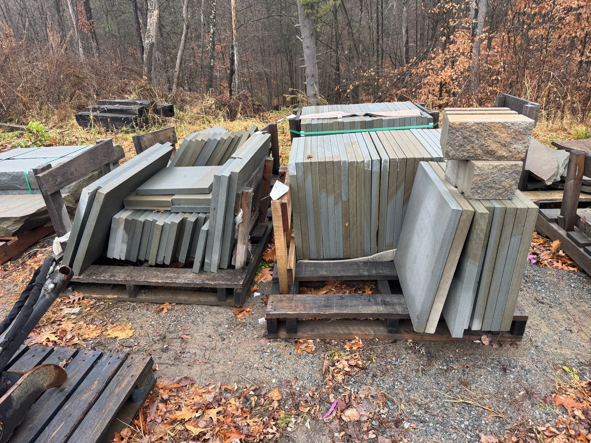 Piles of square, gray stone slabs on wooden pallets outdoors.