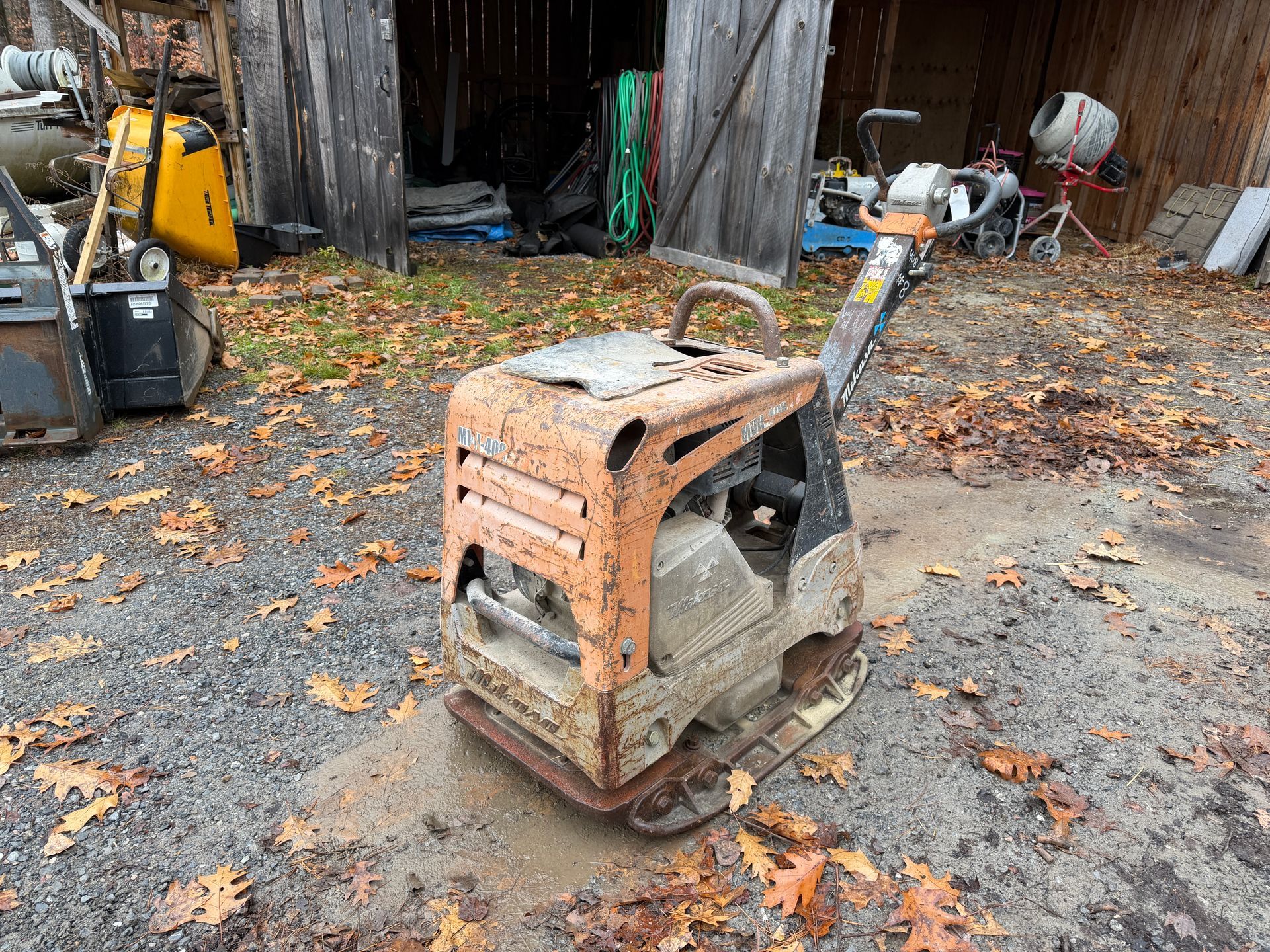 Vibratory plate compactor, orange and black, outdoors on gravel.