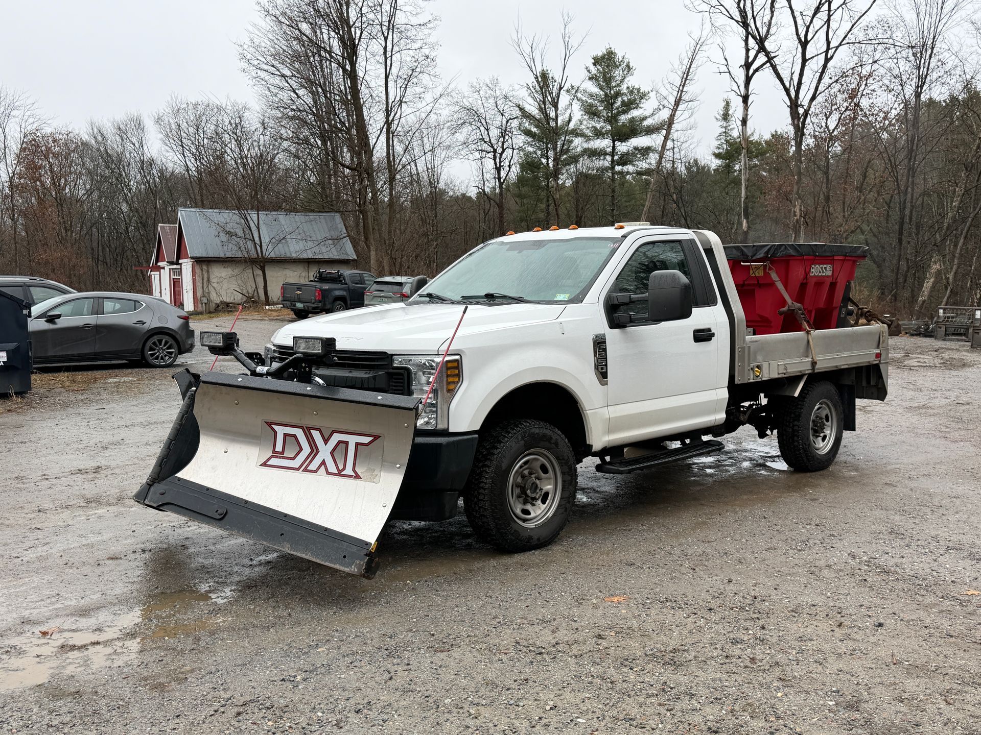 White pickup truck with snowplow and salt spreader parked outside.