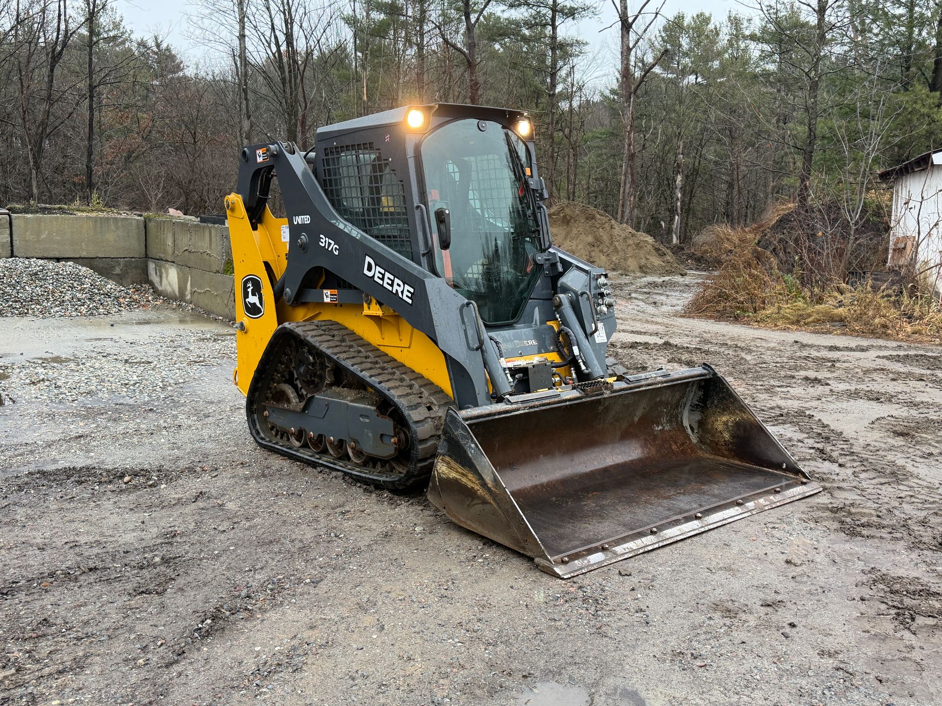 John Deere compact track loader with bucket on a muddy worksite.