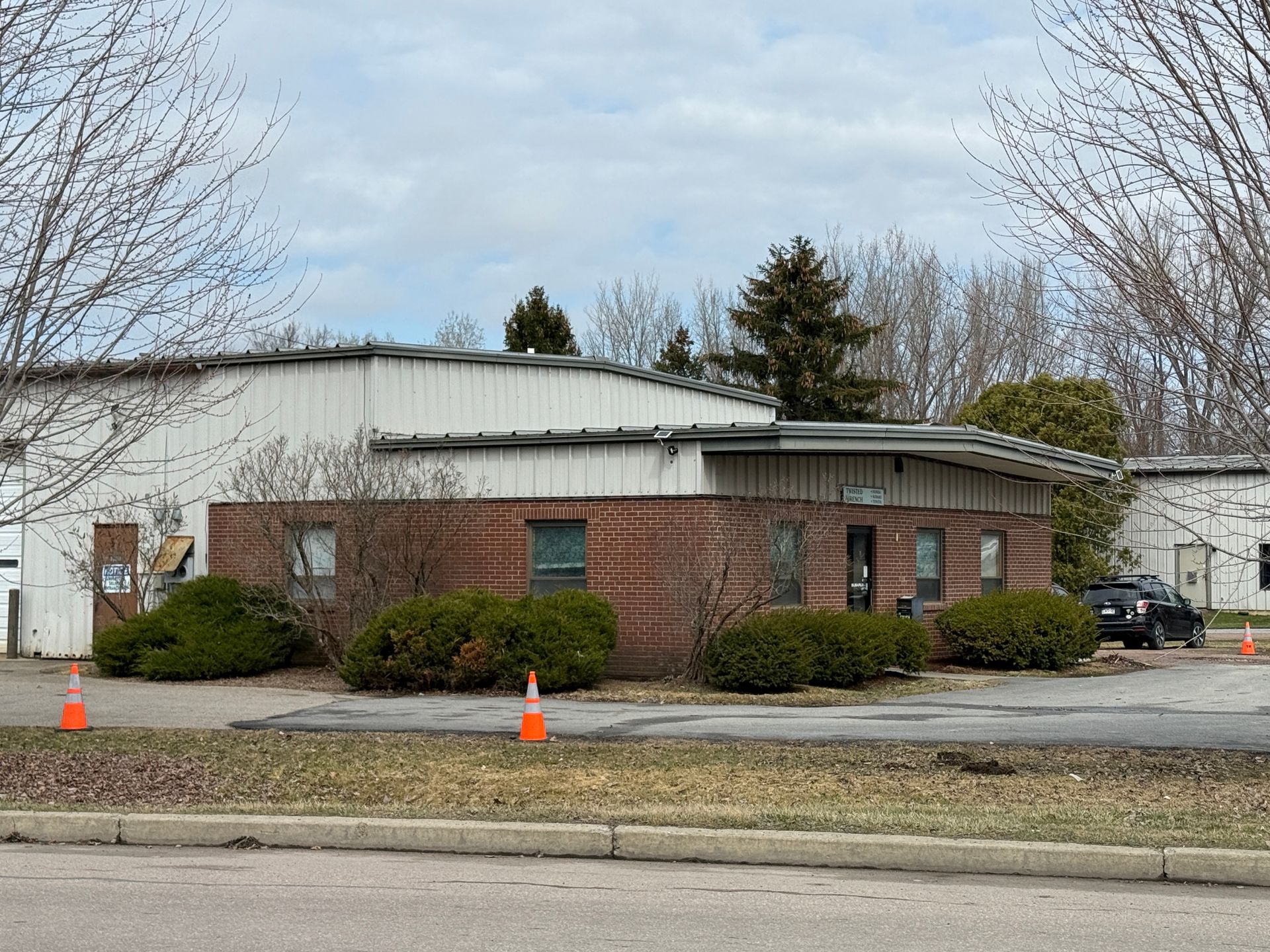 Brick industrial building with white metal roof, small windows, bushes.