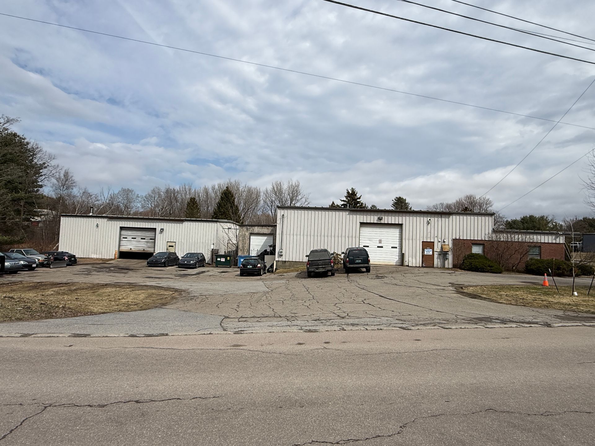 Wide industrial building with parked cars and a gravel lot under a cloudy sky