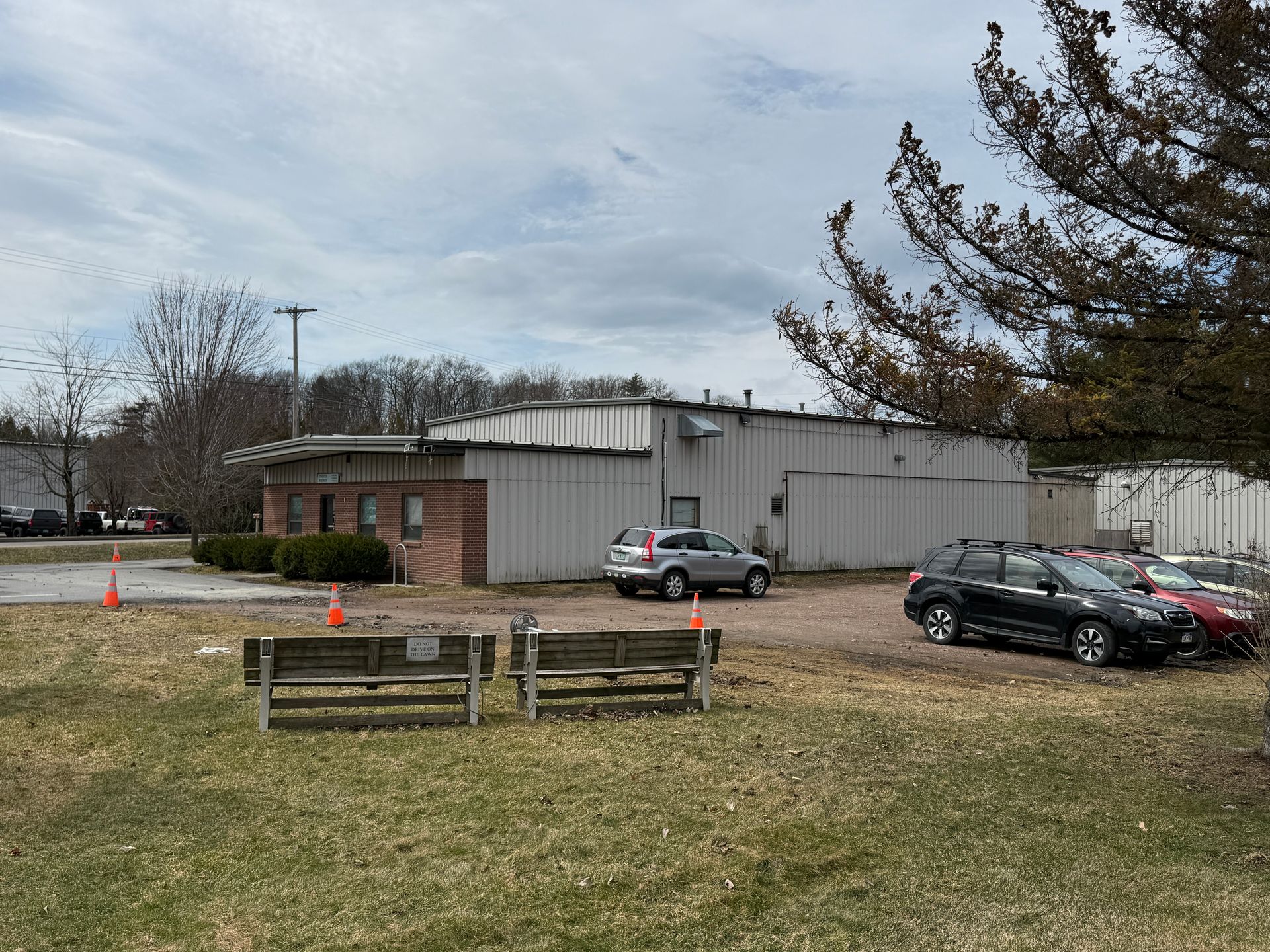 Small brick-and-metal building with parked cars, a wooden bench, and a cloudy sky
