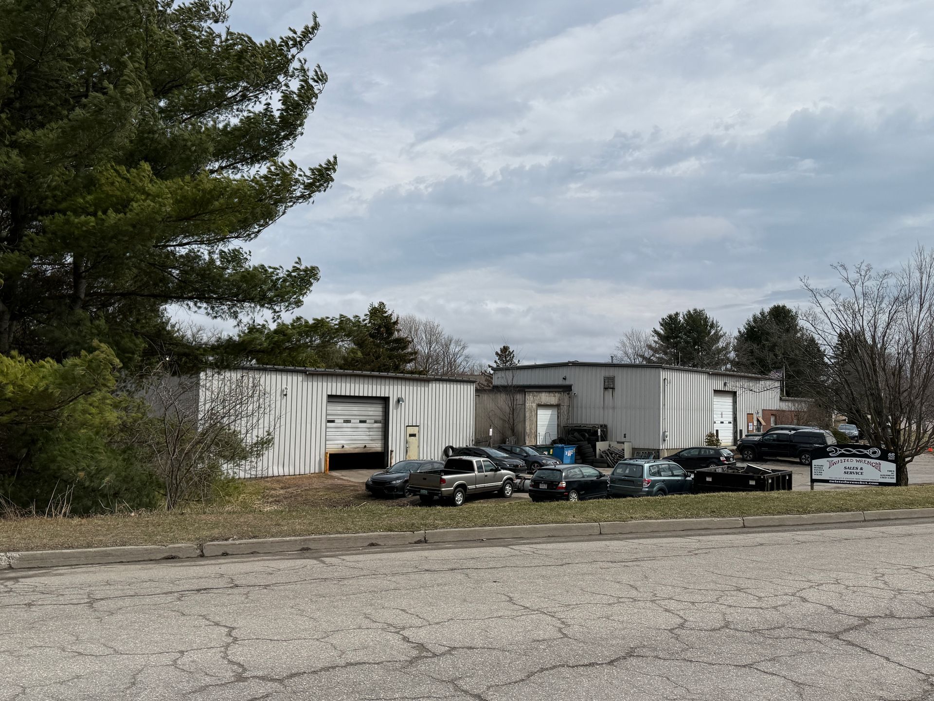 Industrial building with parked vehicles beside a gravel lot under a cloudy sky