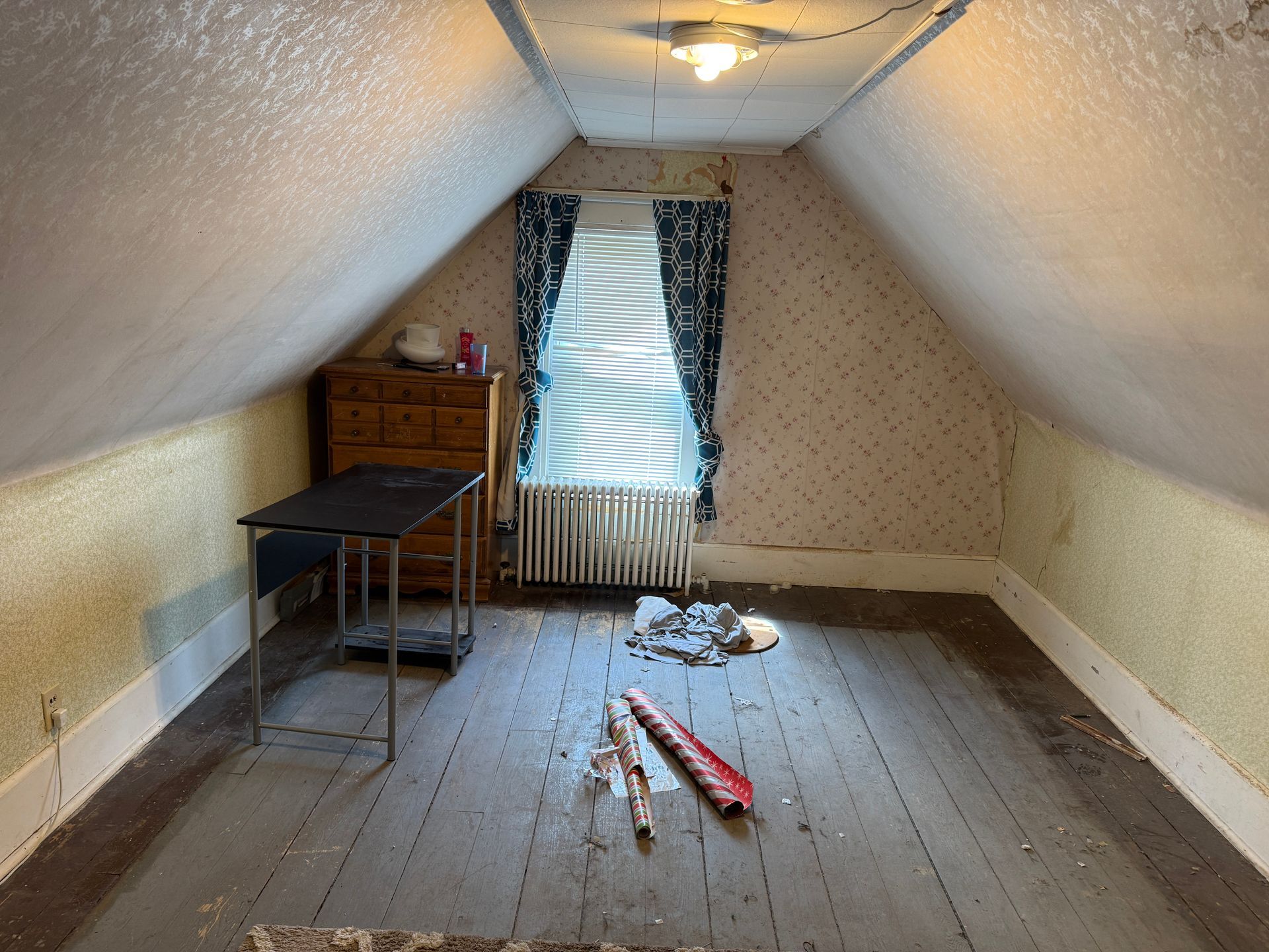 Attic room with sloped ceiling, bare wooden floor, desk, dresser, window