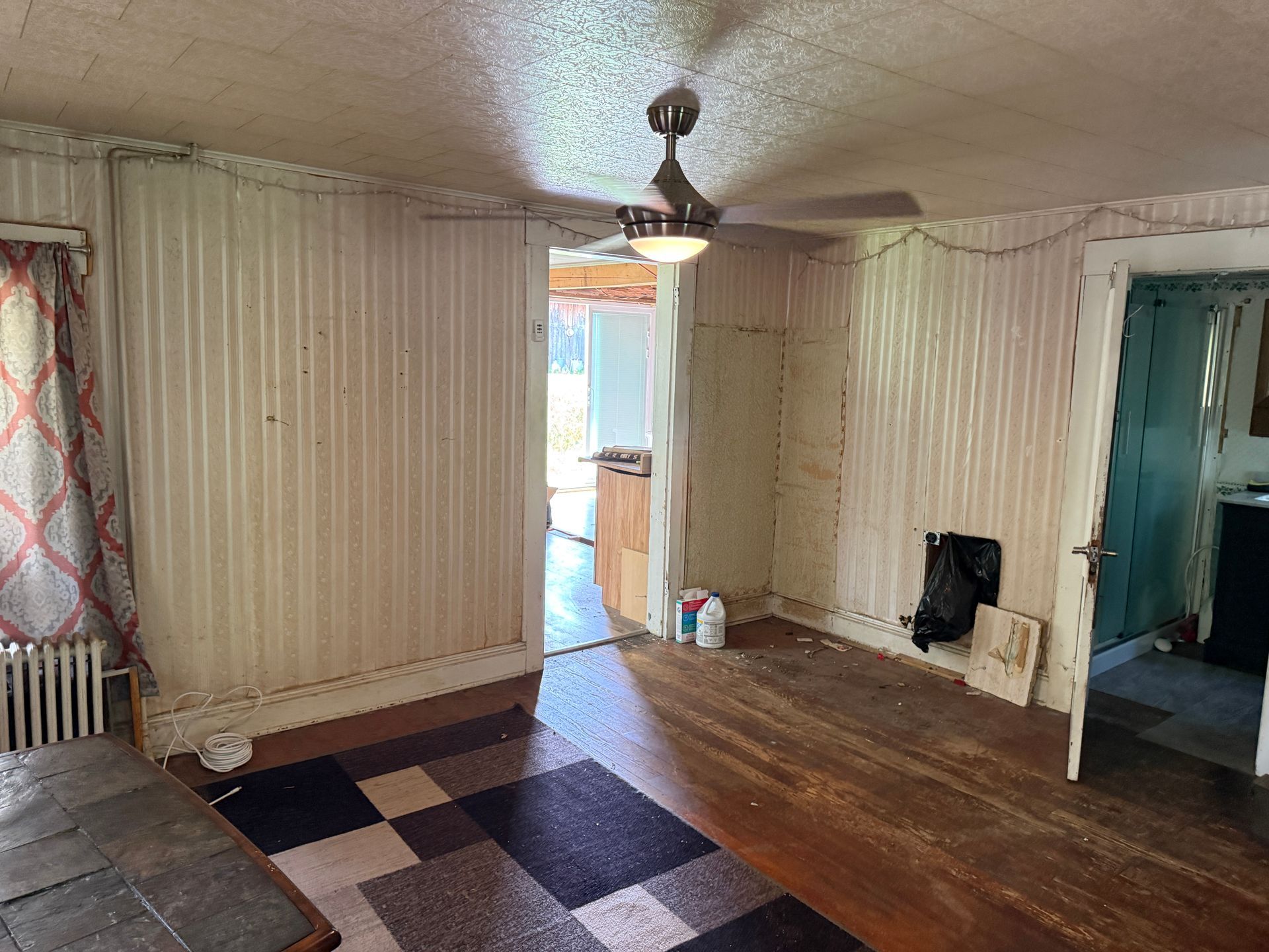 Empty worn room with checkered floor tiles, wood floor, striped walls, and an open doorway to a brighter area