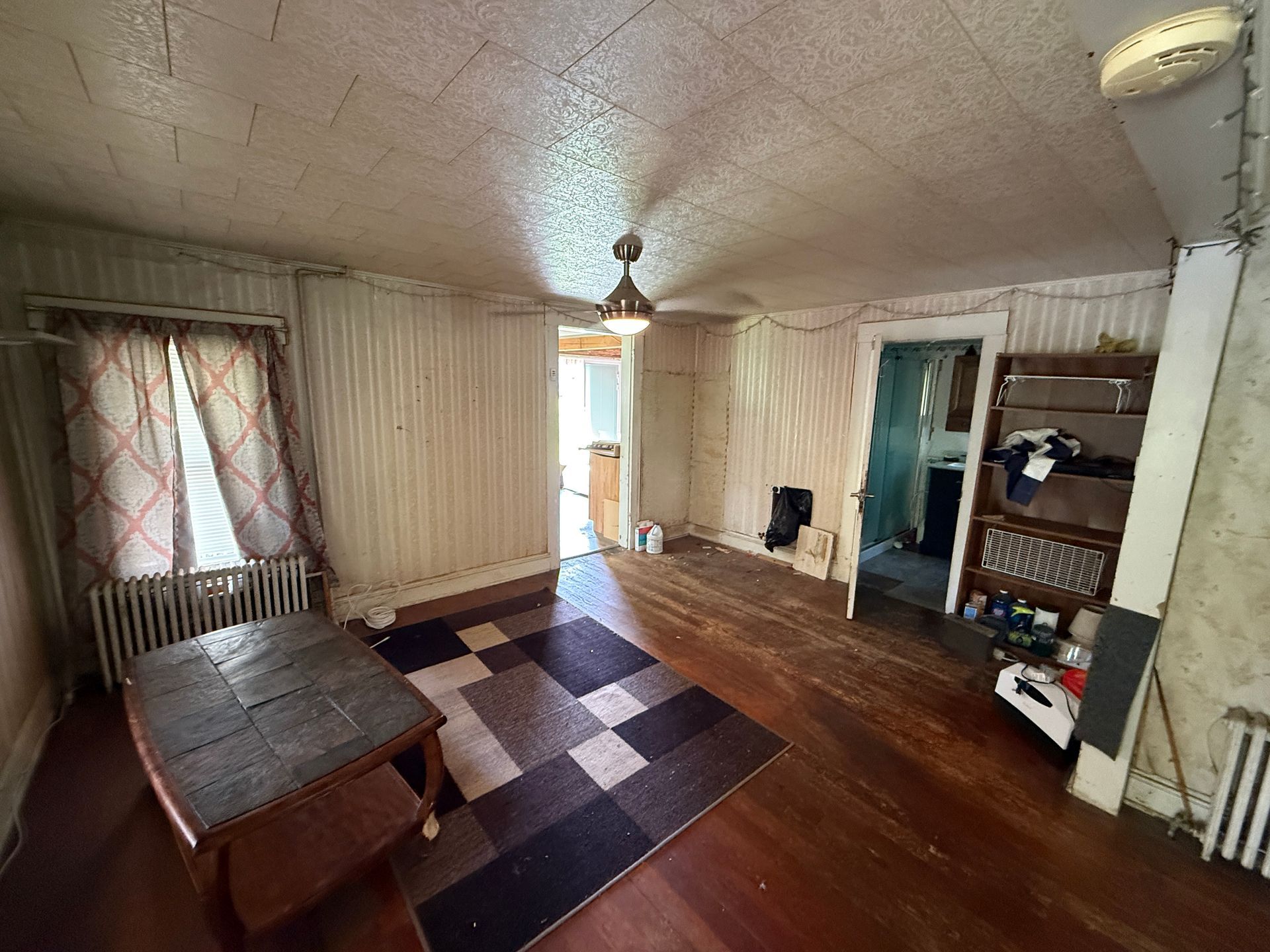 Empty living room with patterned rug, wood floor, radiator, and open shelving by the wall