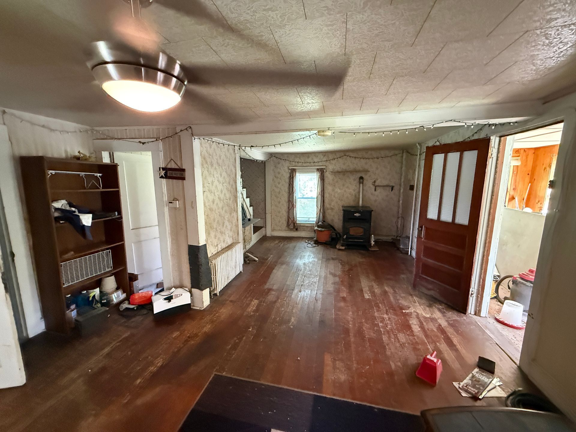 Empty, living room with wooden floor, ceiling light, and open doorway to another room