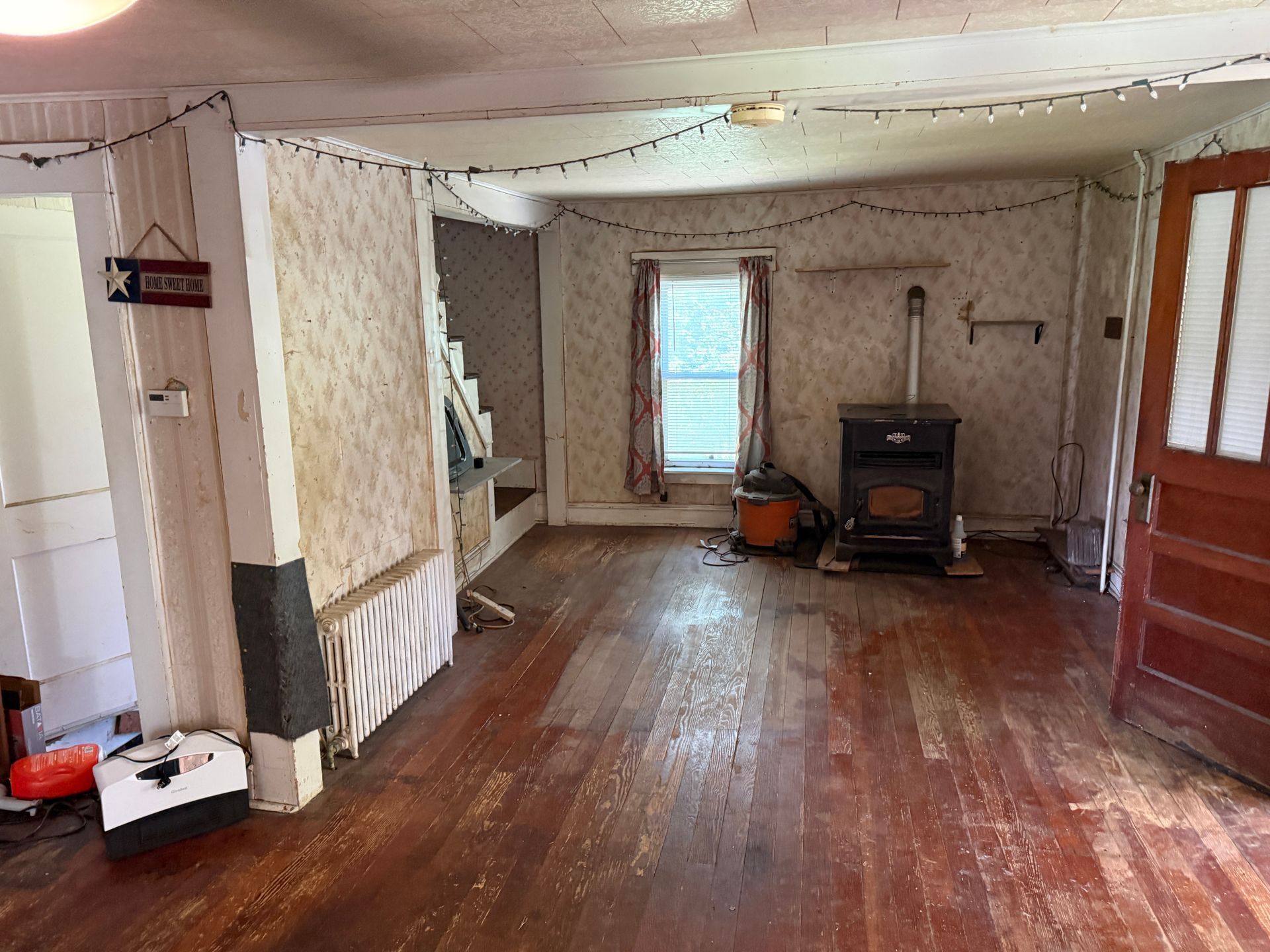 Empty, rustic room with wooden floor, white walls, and a stove near a window.