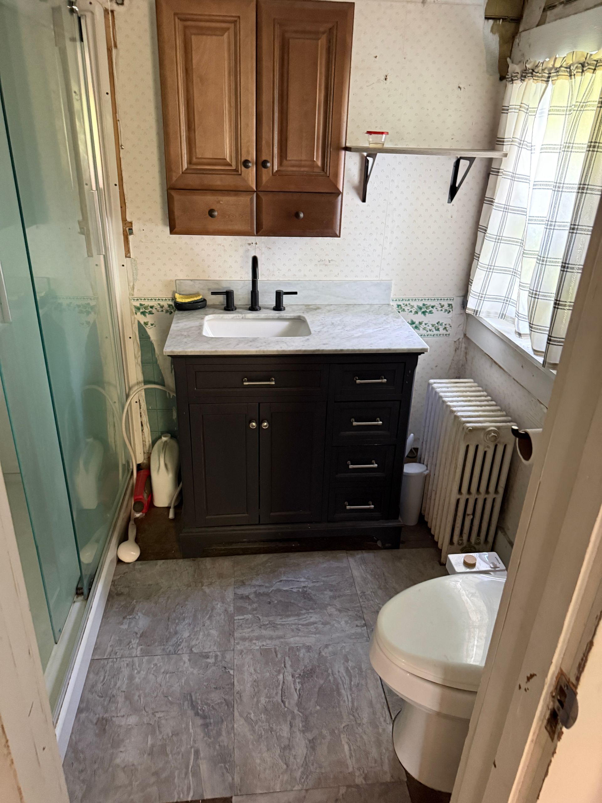 Small bathroom with vanity, sink, mirror cabinet, shower, radiator, and toilet.