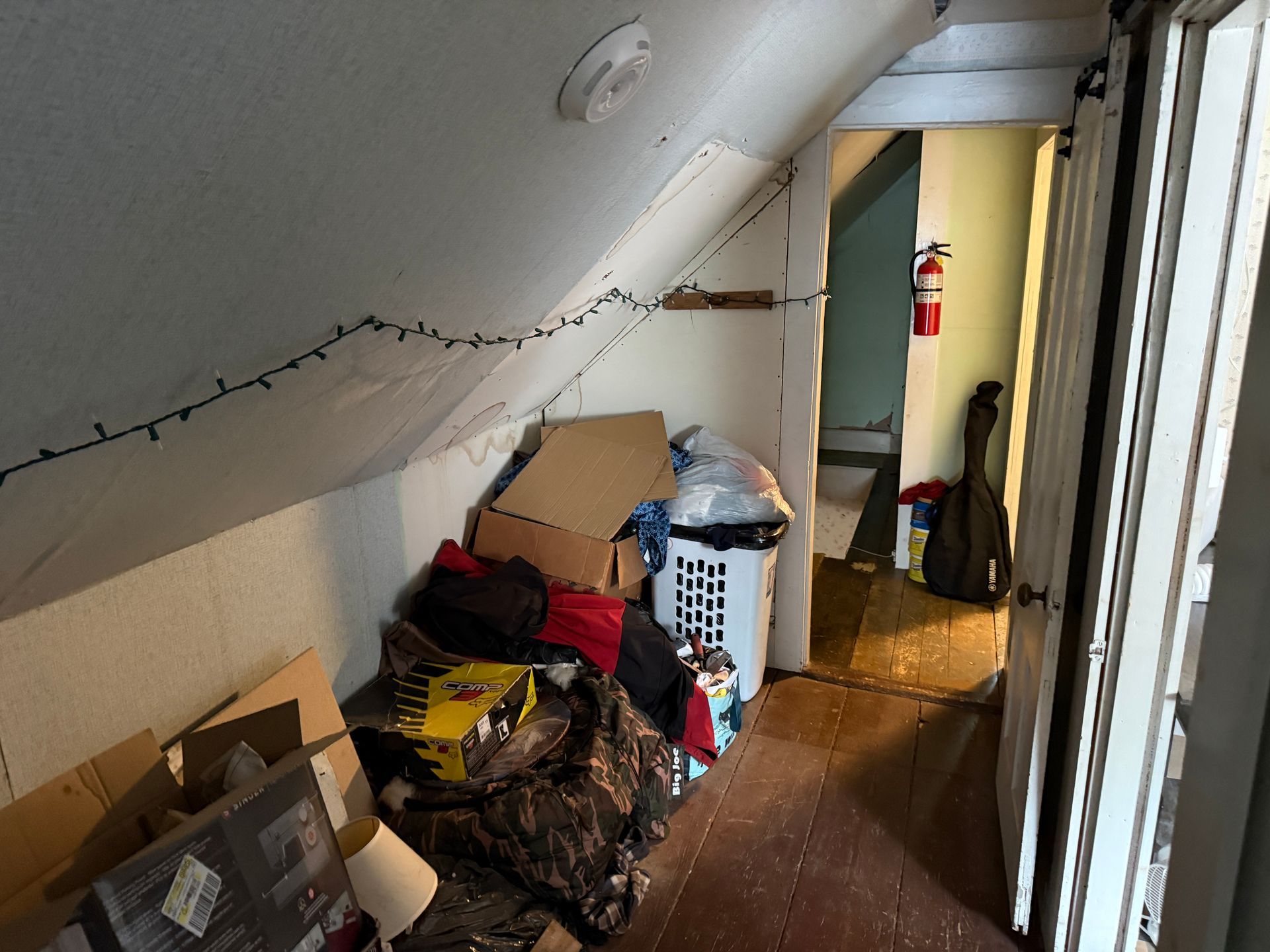 attic hallway with stacked boxes, bags, a laundry basket, and a fire extinguisher by the doorway