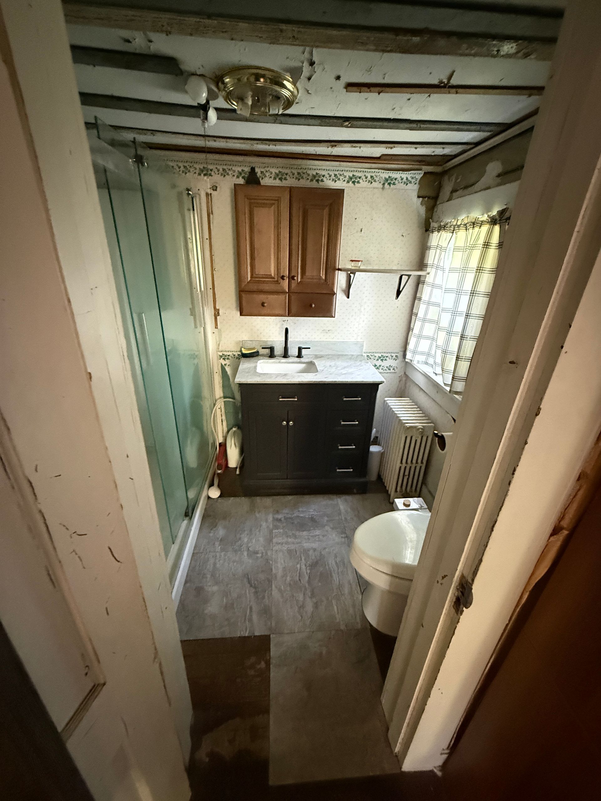 Small bathroom with a vanity, toilet, window, and green walls seen through an open doorway.