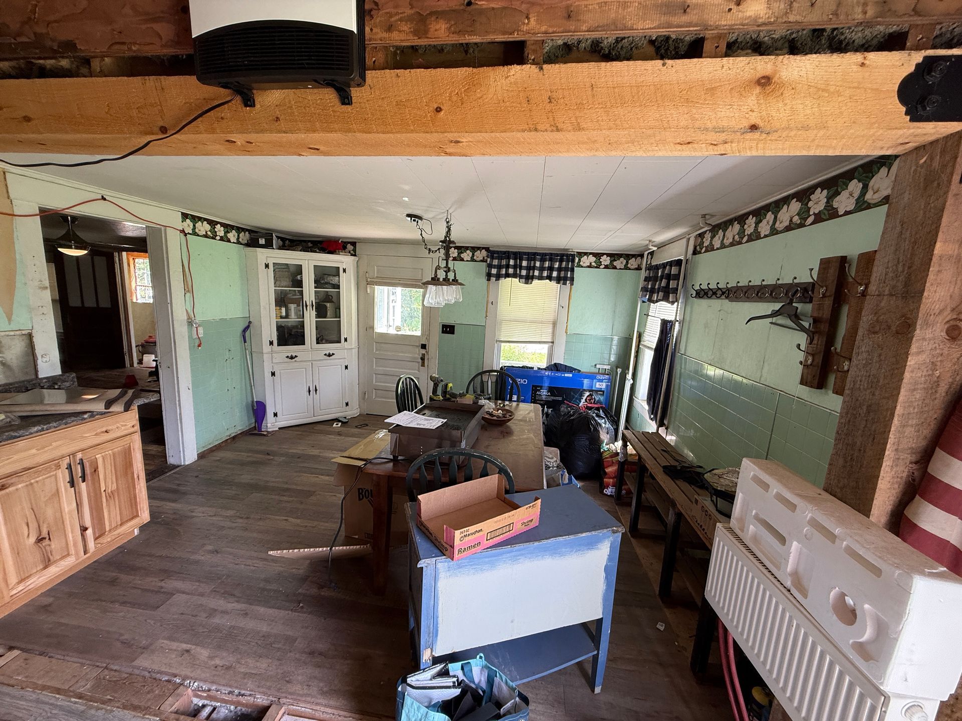 rustic kitchen and living area with wood beams, white cabinets, and a washing machine on the right.