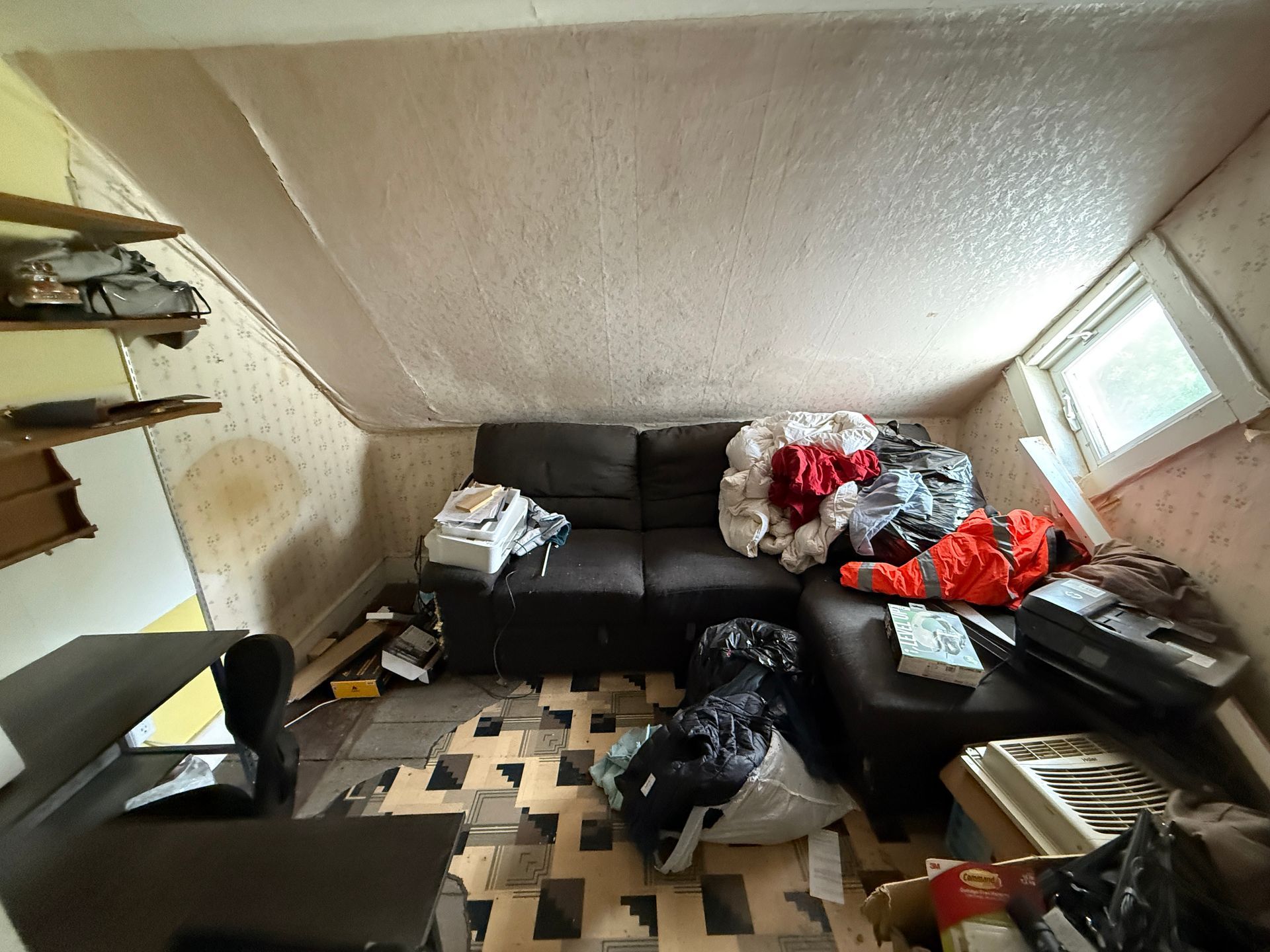 living room with a black sofa, and a small window on the right.