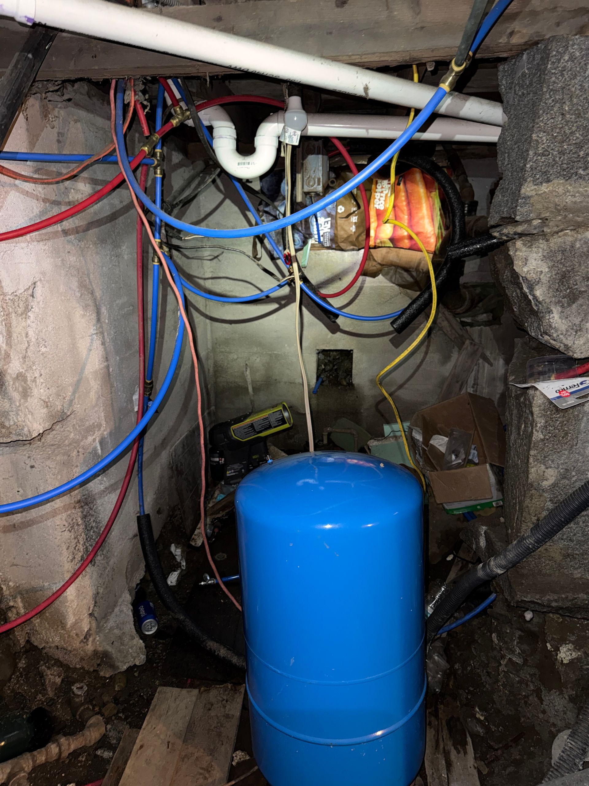 Blue tank and exposed wiring in a basement utility space with pipes and a lit fixture
