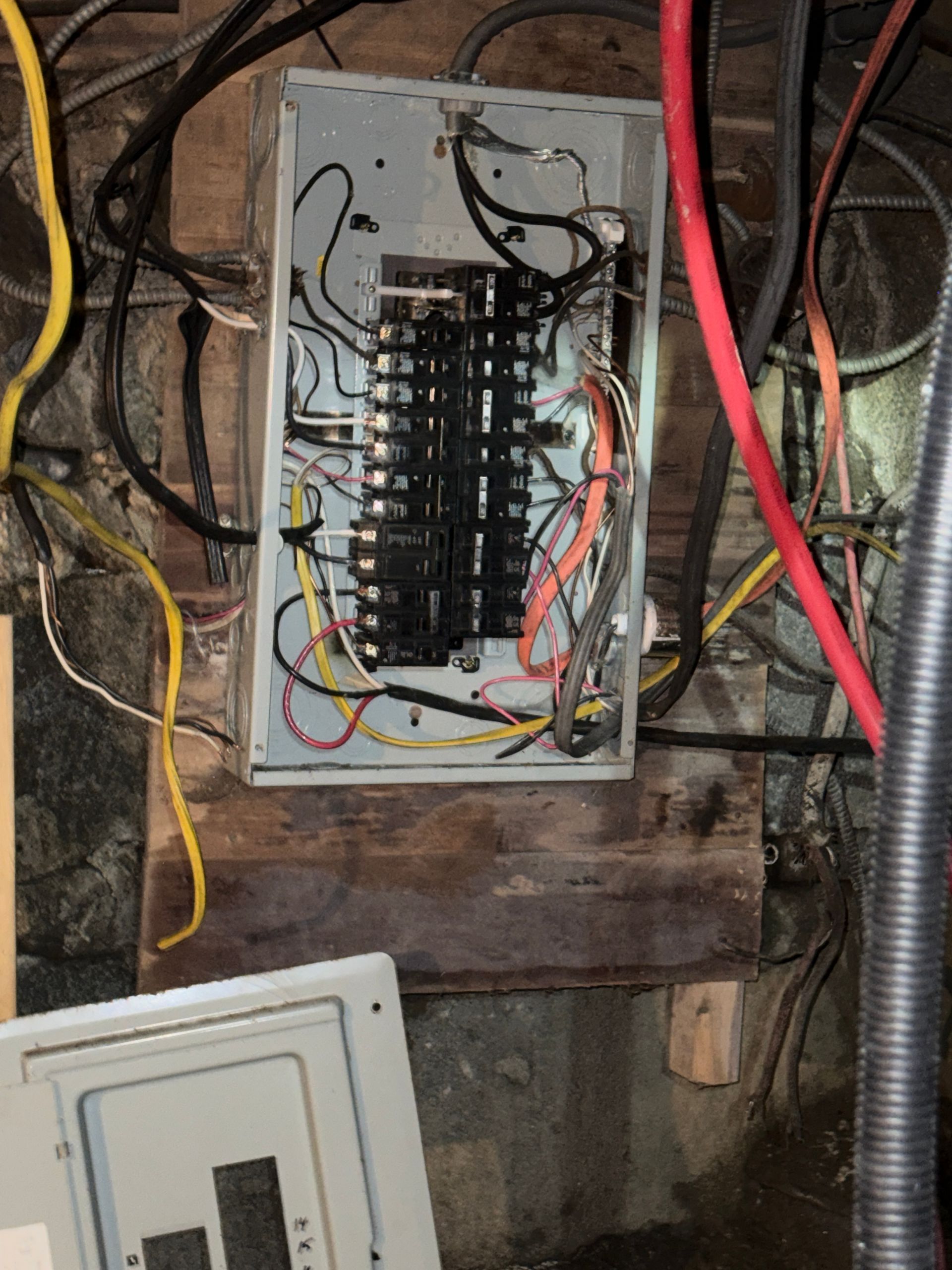 Open electrical breaker panel with exposed wiring in a basement utility area