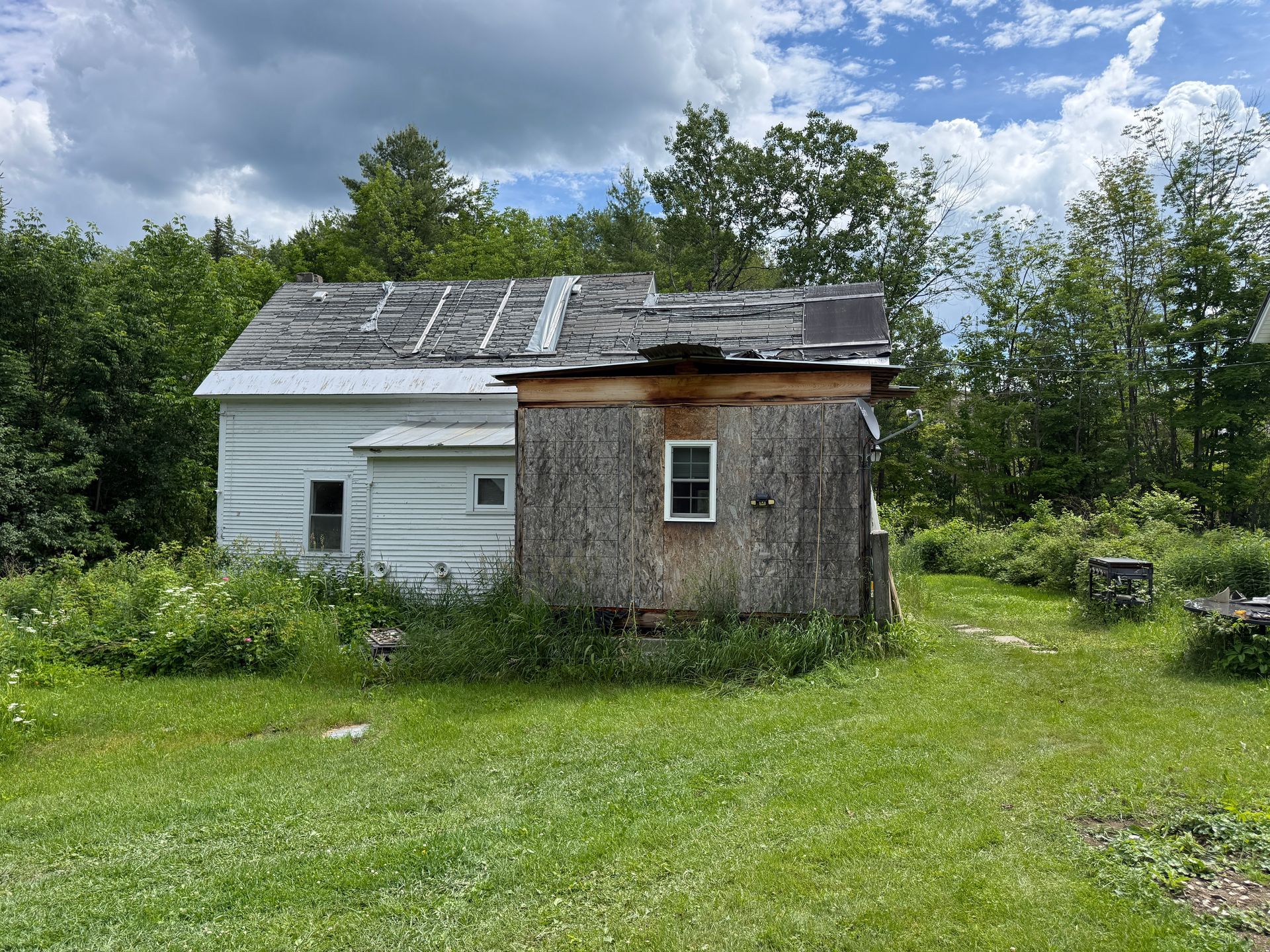 Small house with a patchwork roof in a grassy field under cloudy skies