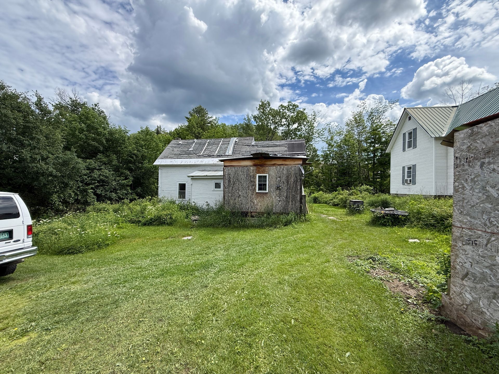 Grassy backyard with a small shed, white house, and cloudy sky