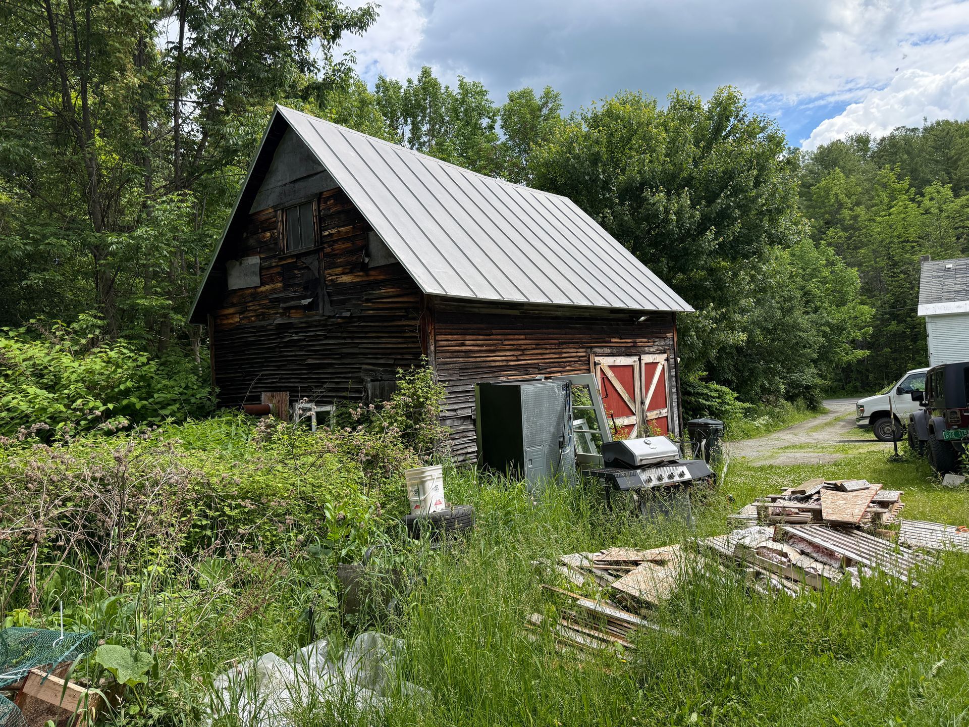 Rustic wooden barn with metal roof in a grassy yard, surrounded by trees