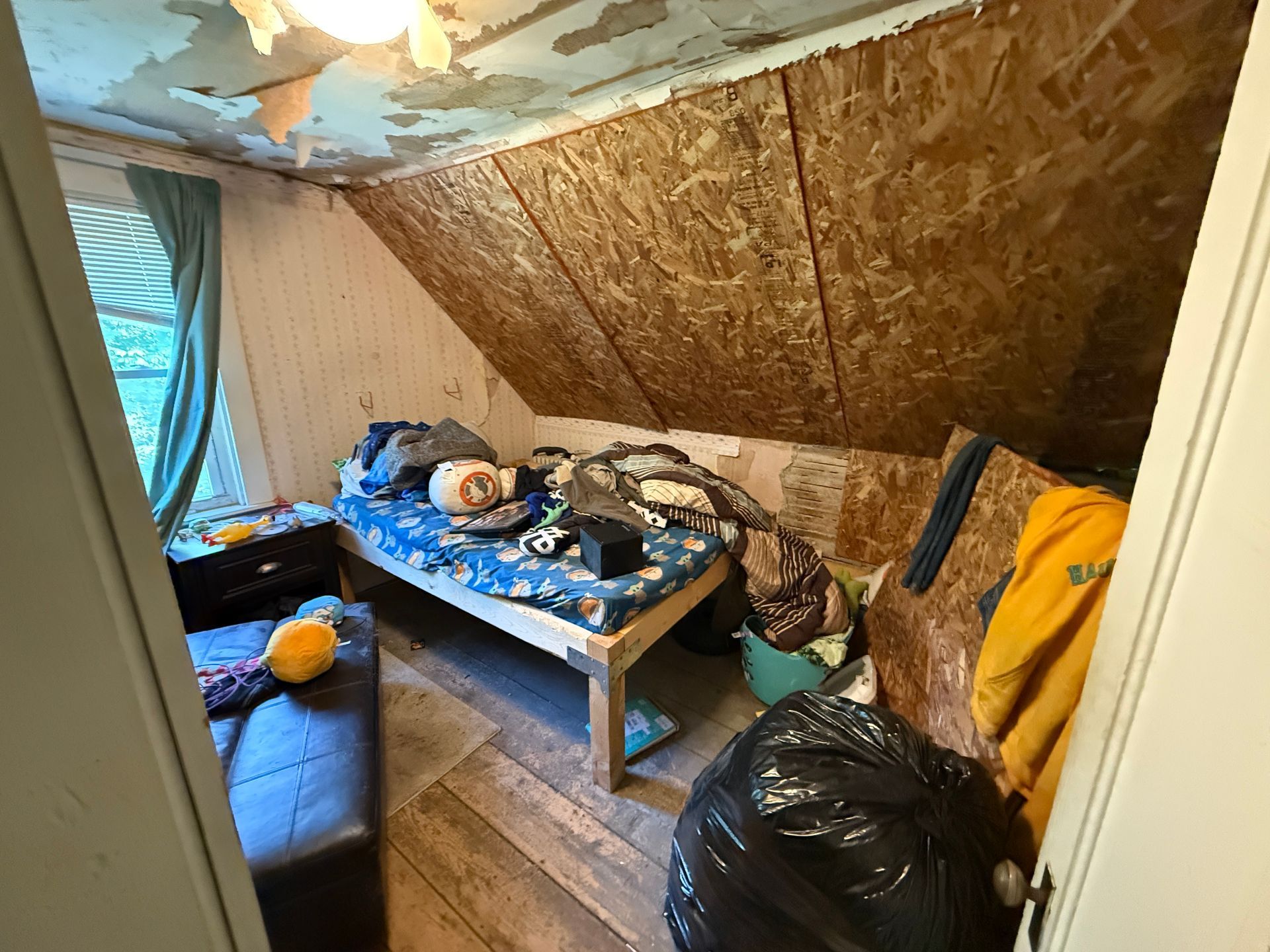 An attic room with a couch, low table, bags, and a sloped ceiling with paint.
