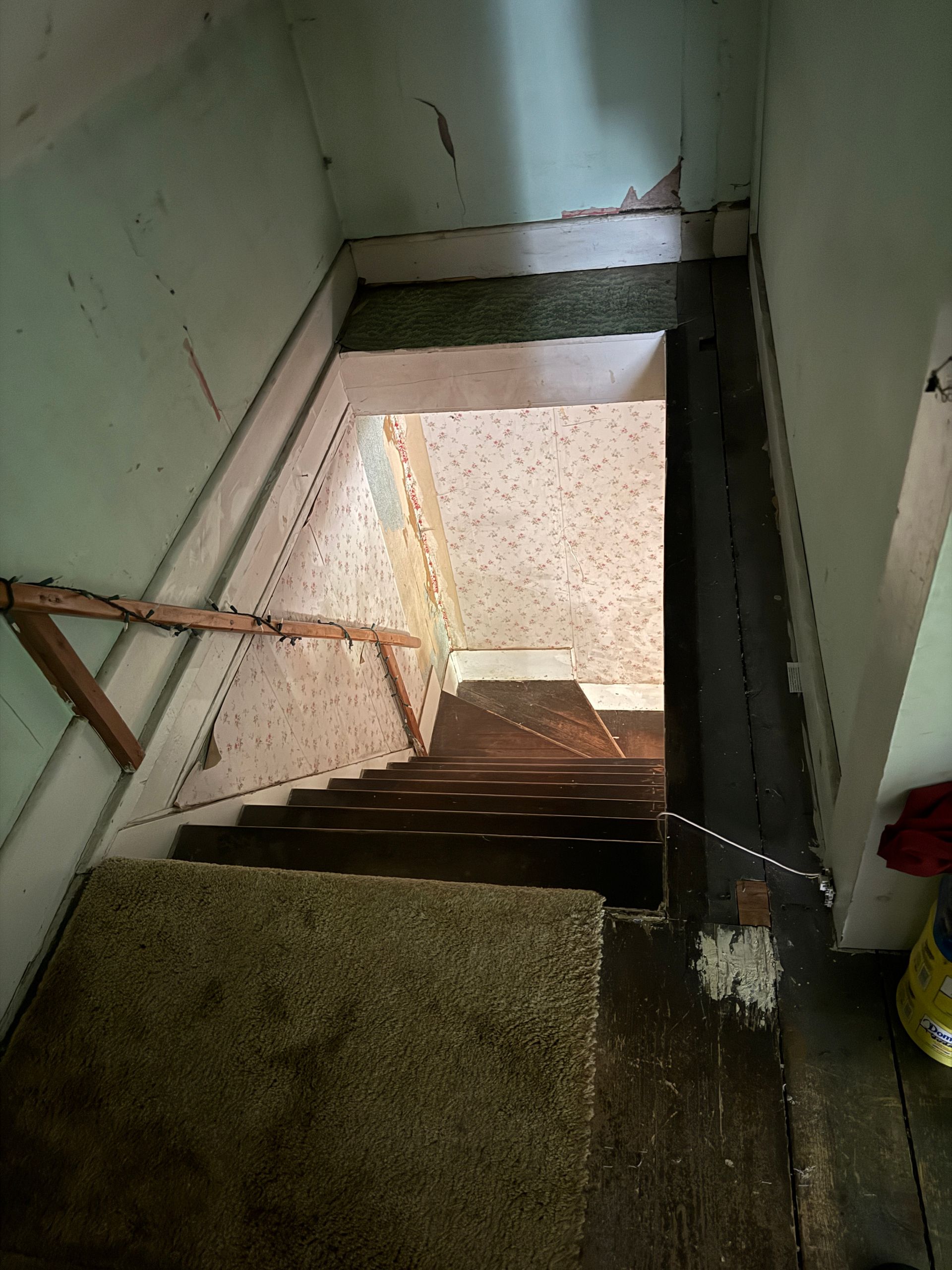 Narrow stairwell with green walls and wooden handrail descending to a lower floor