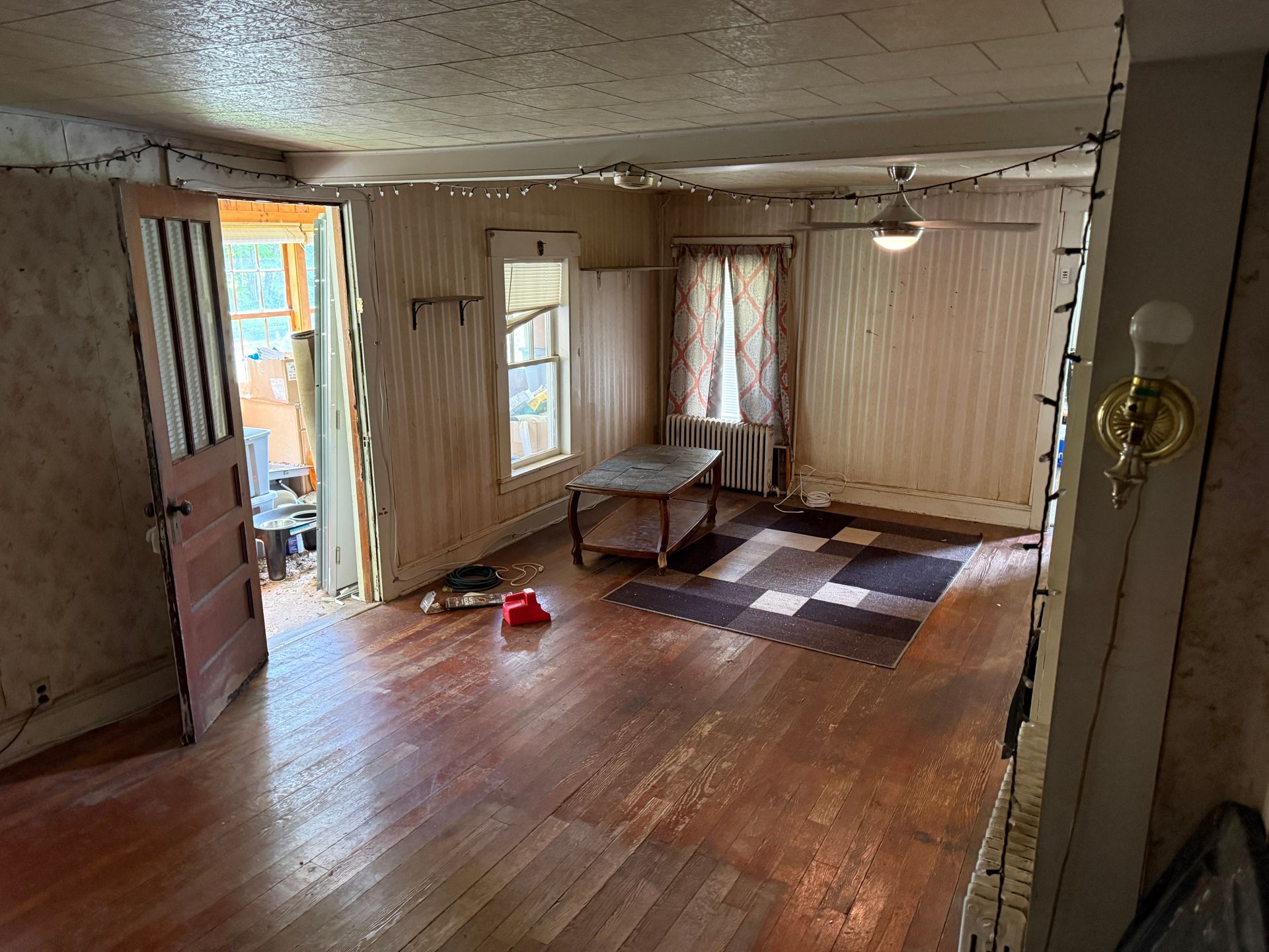 Empty living room with wood floors, striped walls, a small couch, and daylight through the open door and window