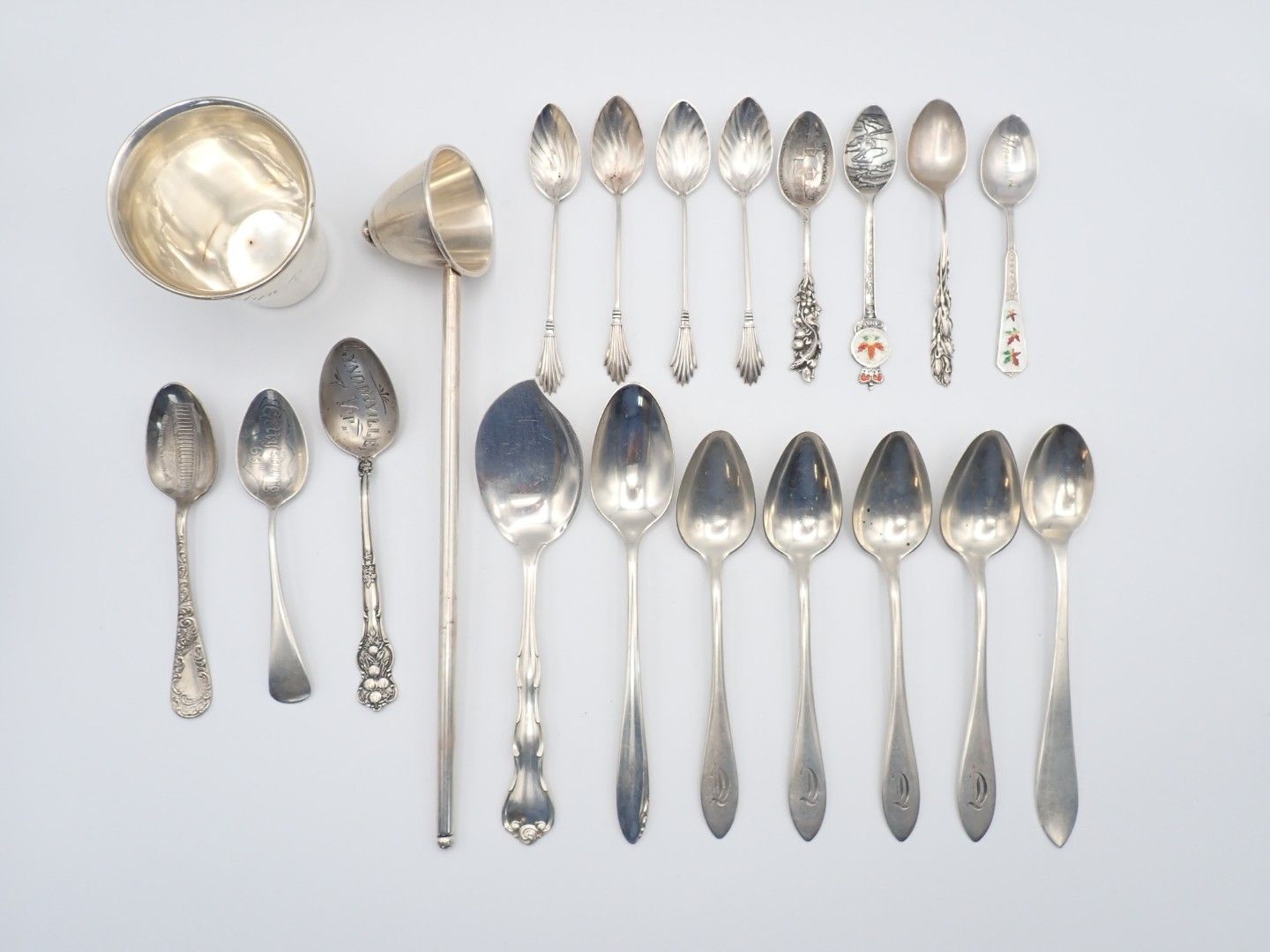 Assorted silver spoons and a small cup arranged on a white background.