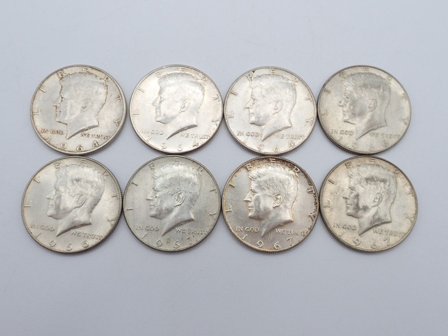 Eight worn silver-colored coins arranged in two rows on a light background