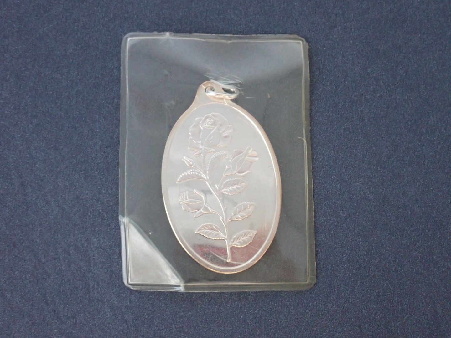 Silver oval pendant with floral engraving in a clear plastic sleeve