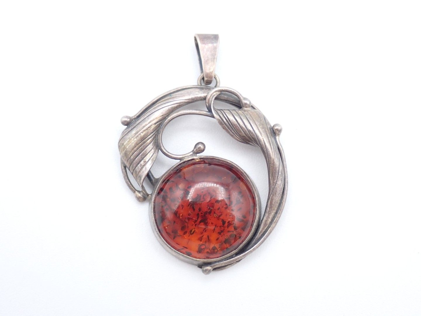 Silver pendant with a red round gemstone and swirling vine-like design