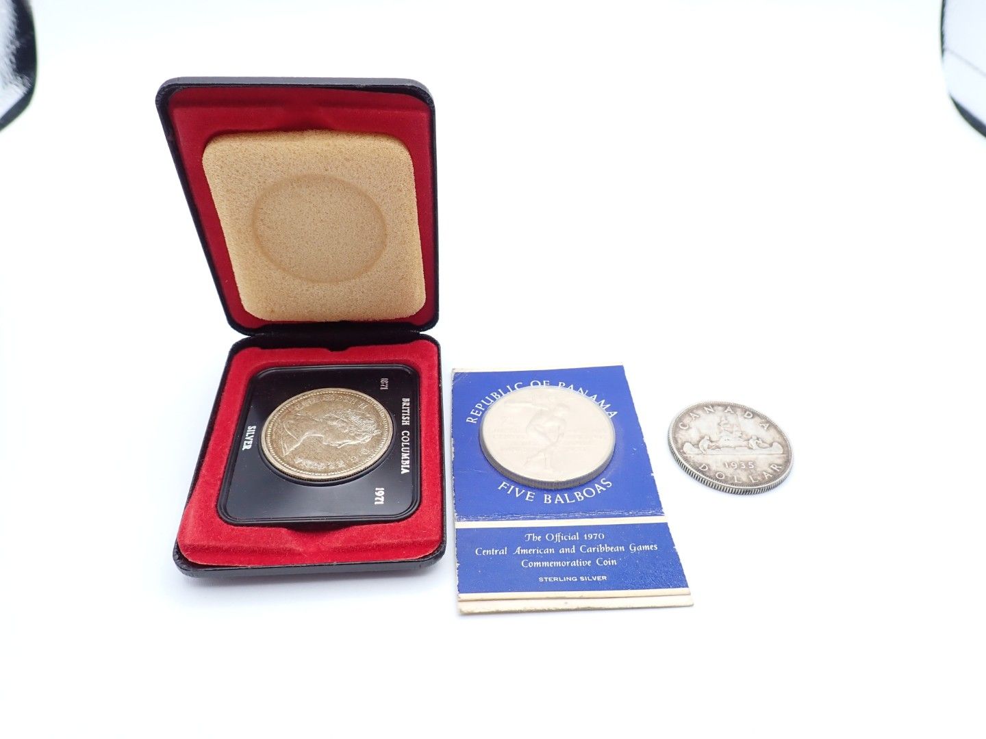 Red coin case with a medal, blue booklet, and loose silver coin on a white background