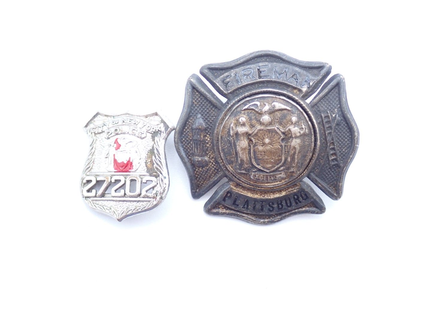 Two metal badges, one small silver badge and one larger dark badge, displayed side by side.