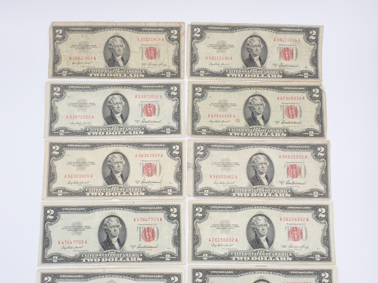 Eight two-dollar bills arranged in two vertical columns on a white surface.