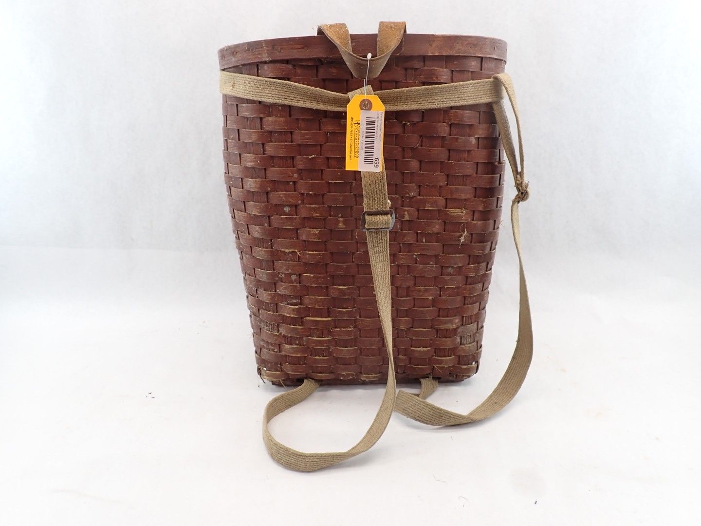 Brown woven basket with a long shoulder strap and a yellow tag on a white background
