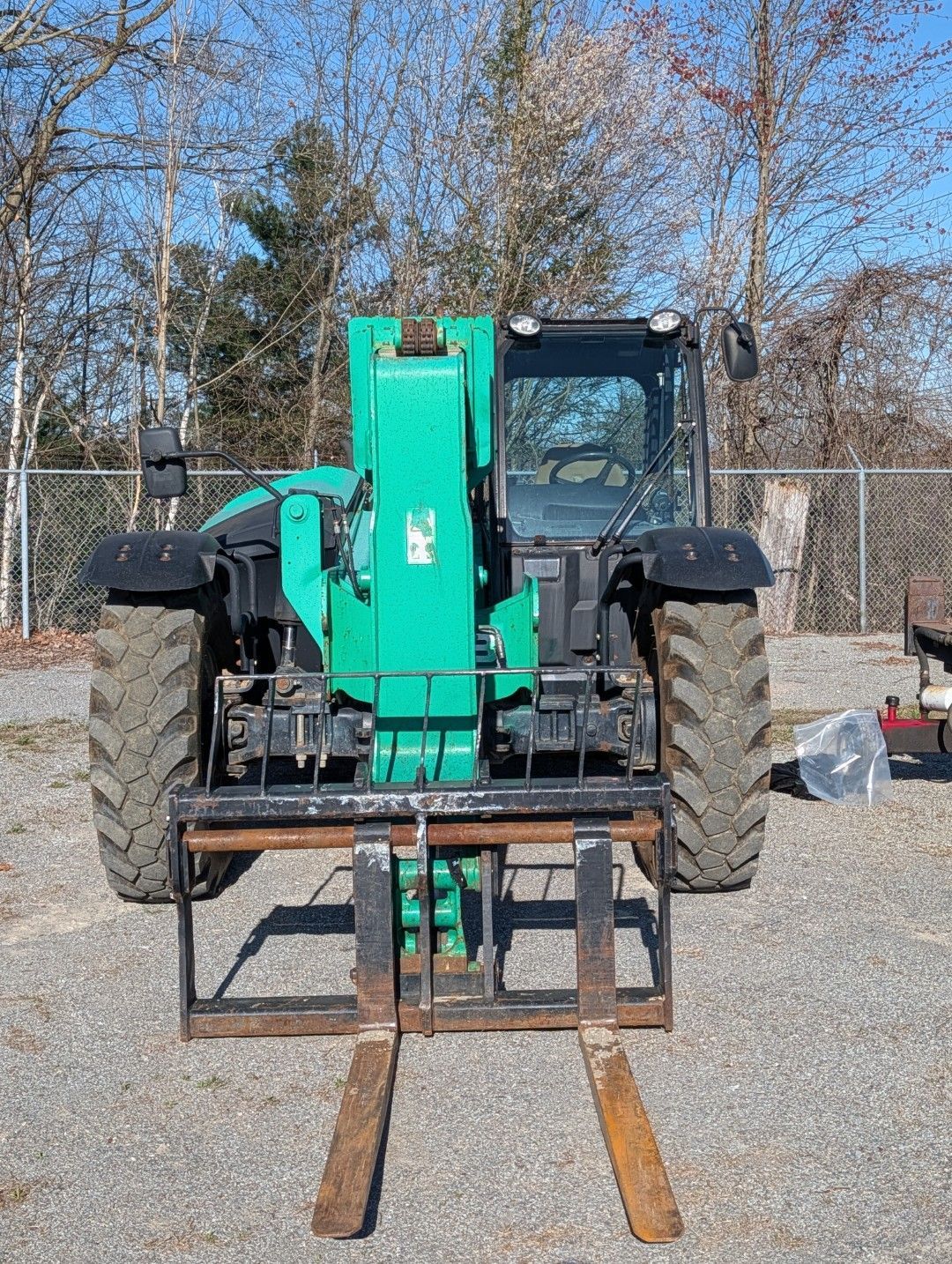 Front view of a turquoise tractor with forks