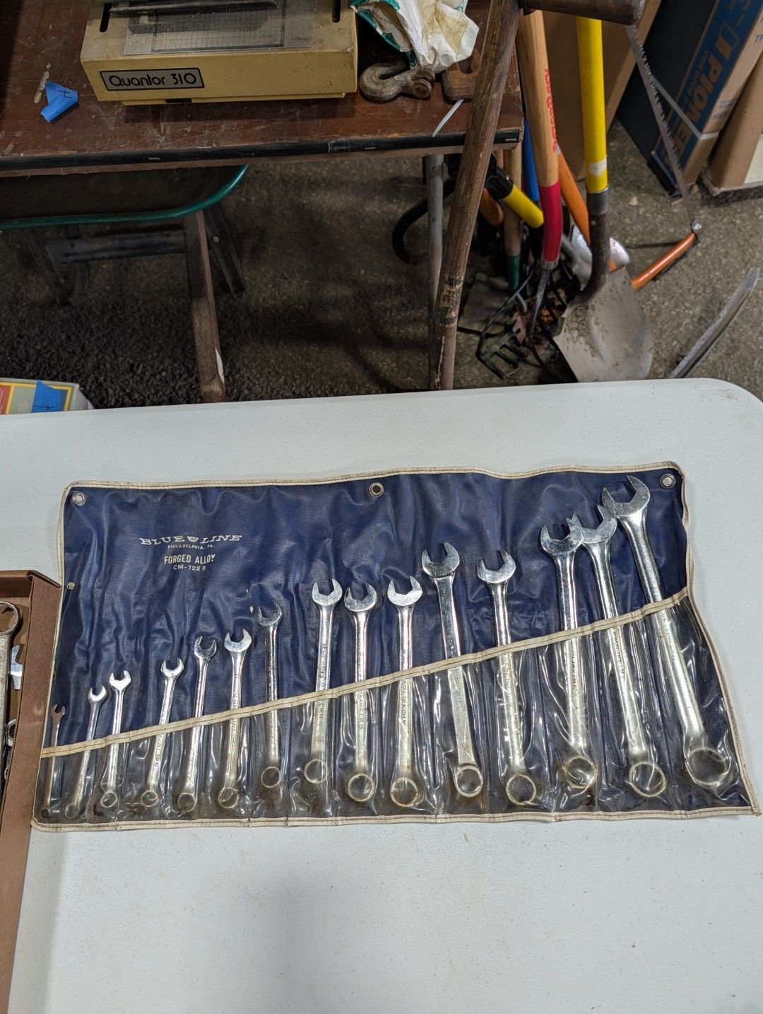 A blue roll-up tool pouch with several silver wrenches arranged on a table.