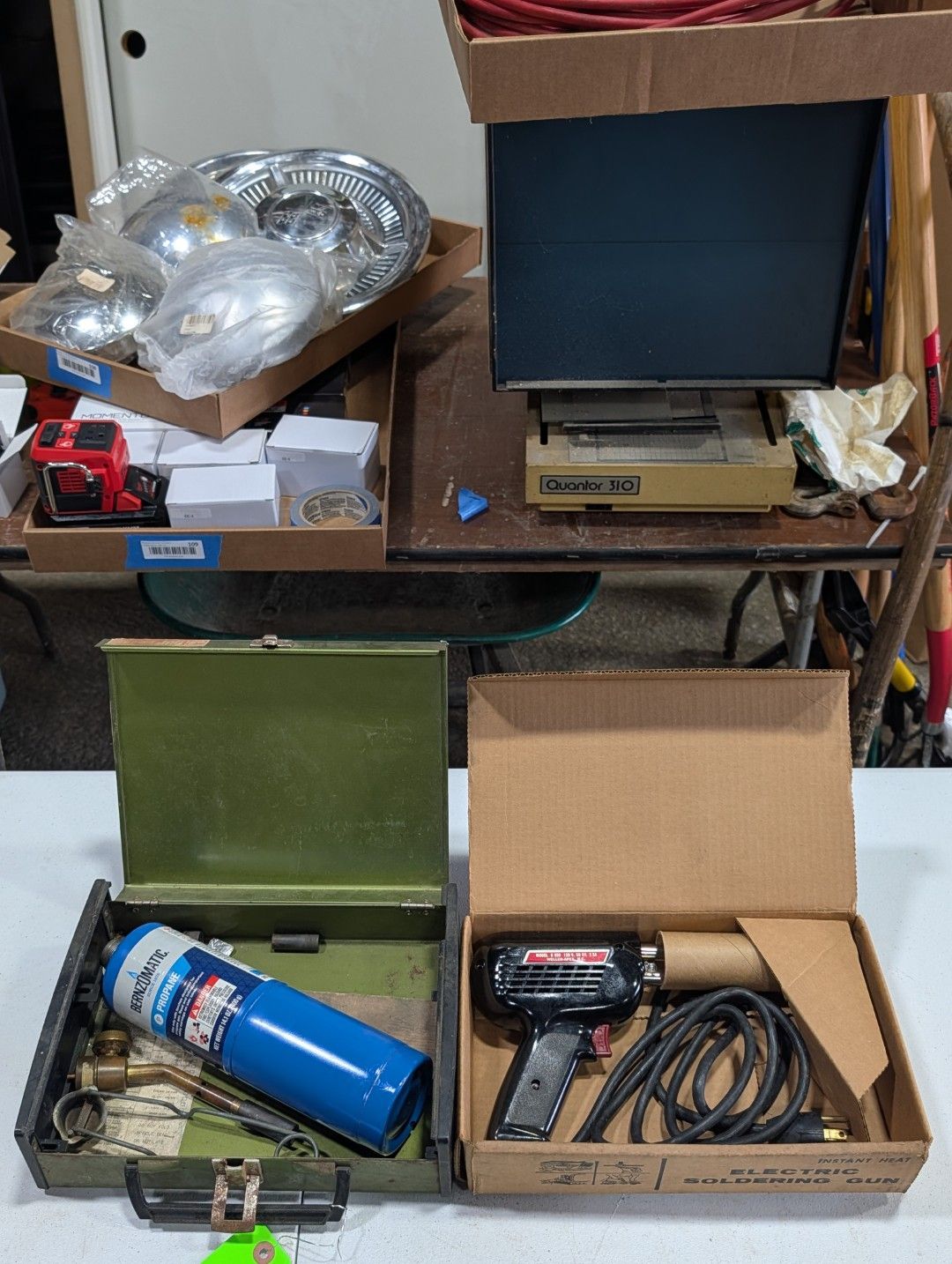 Open boxes of assorted tools and parts on shelves, including a blue canister, wires, and a metal dish.