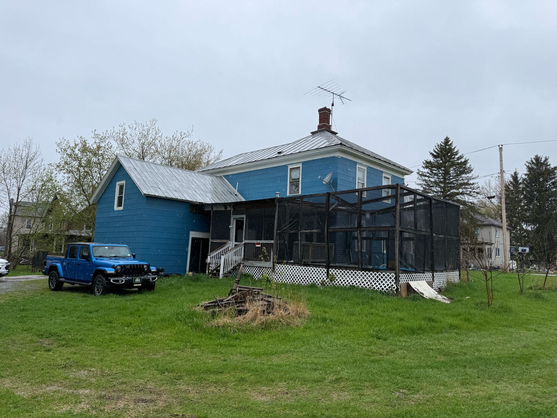 Blue house with a black screened porch, a blue truck, and a grassy yard under an overcast sky