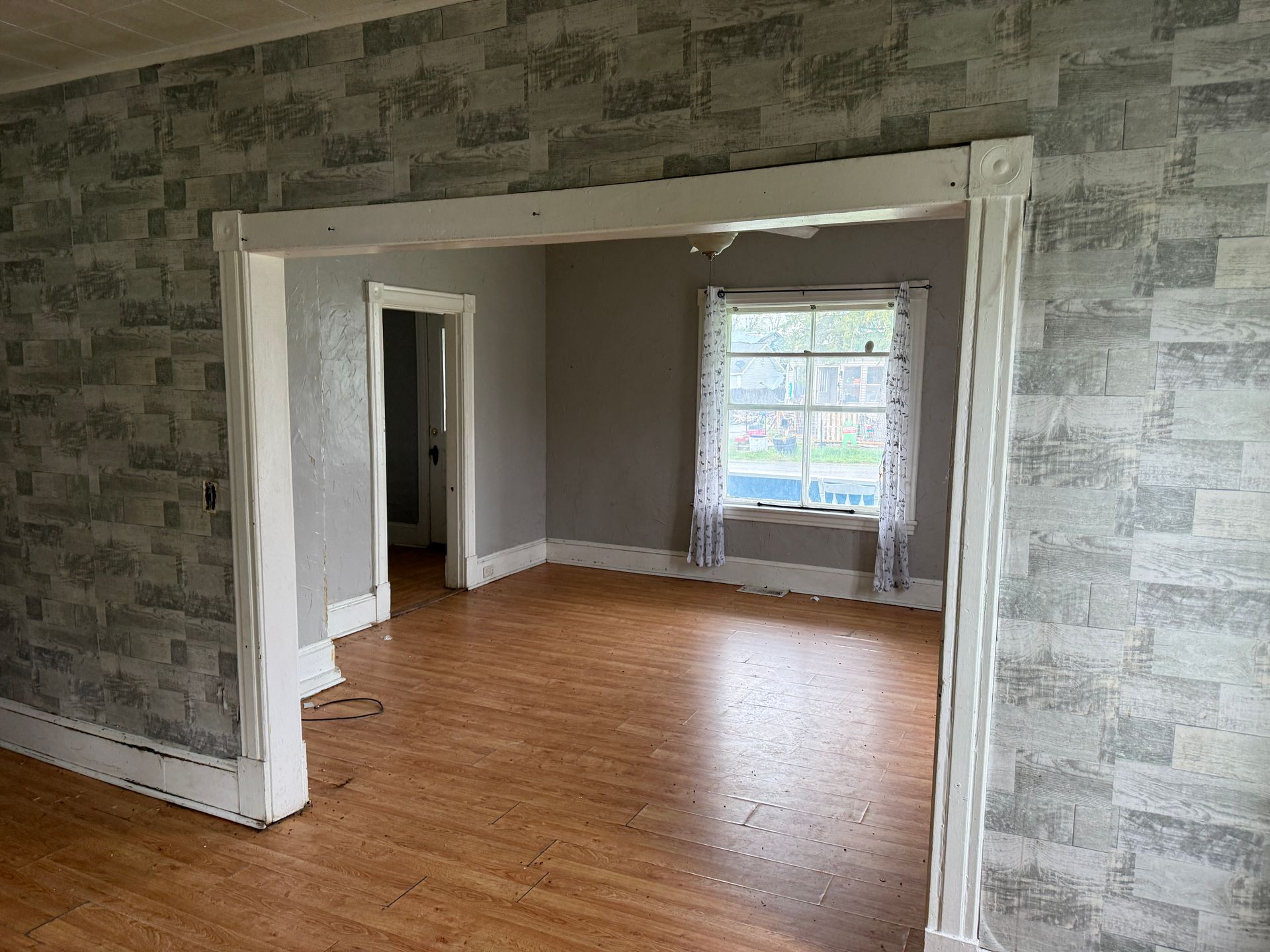 Empty room with hardwood floors, gray patterned walls, and a large window in the back.