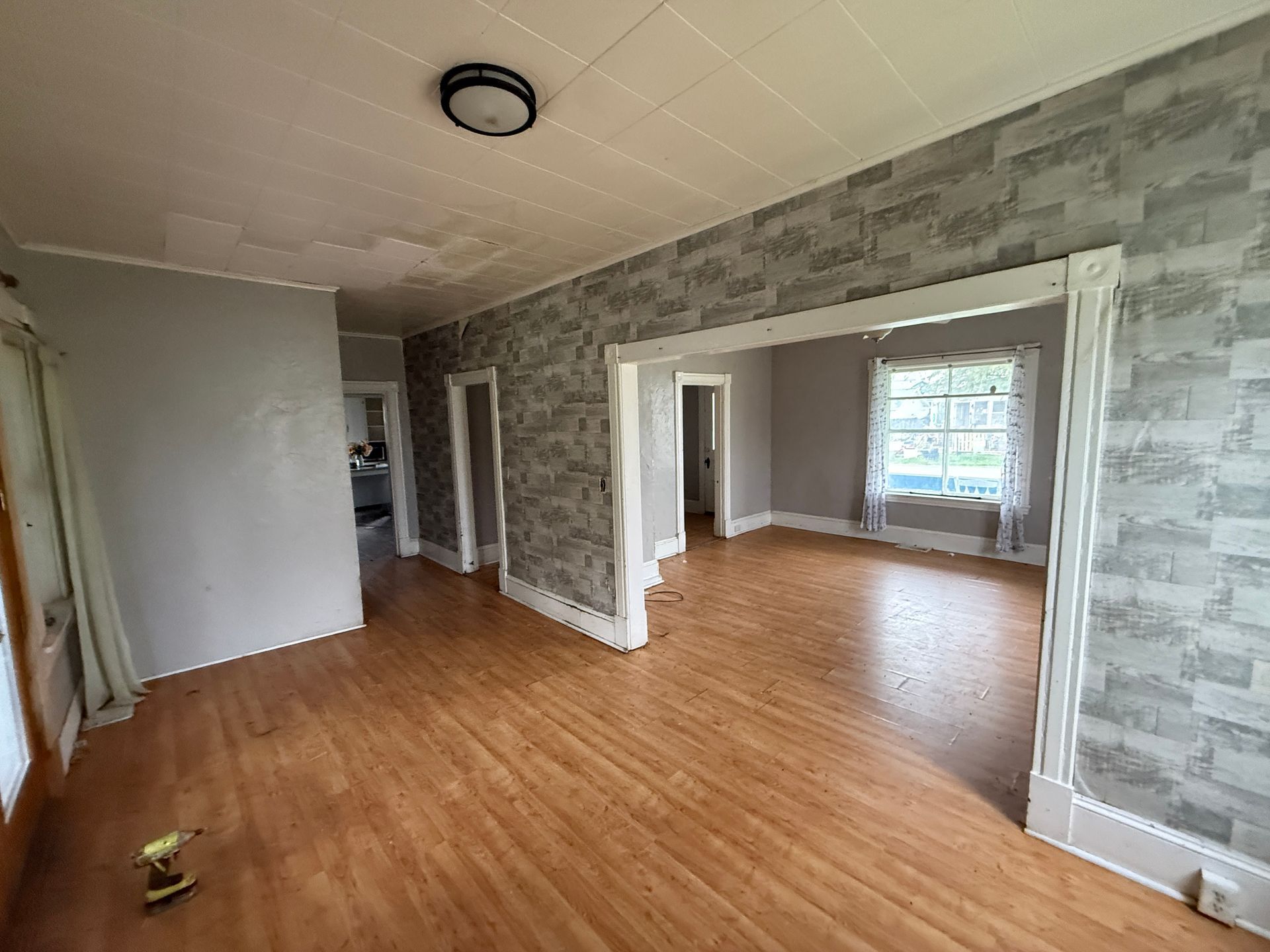 Empty living room with wood floors, gray walls, and large doorway to a second room with windows