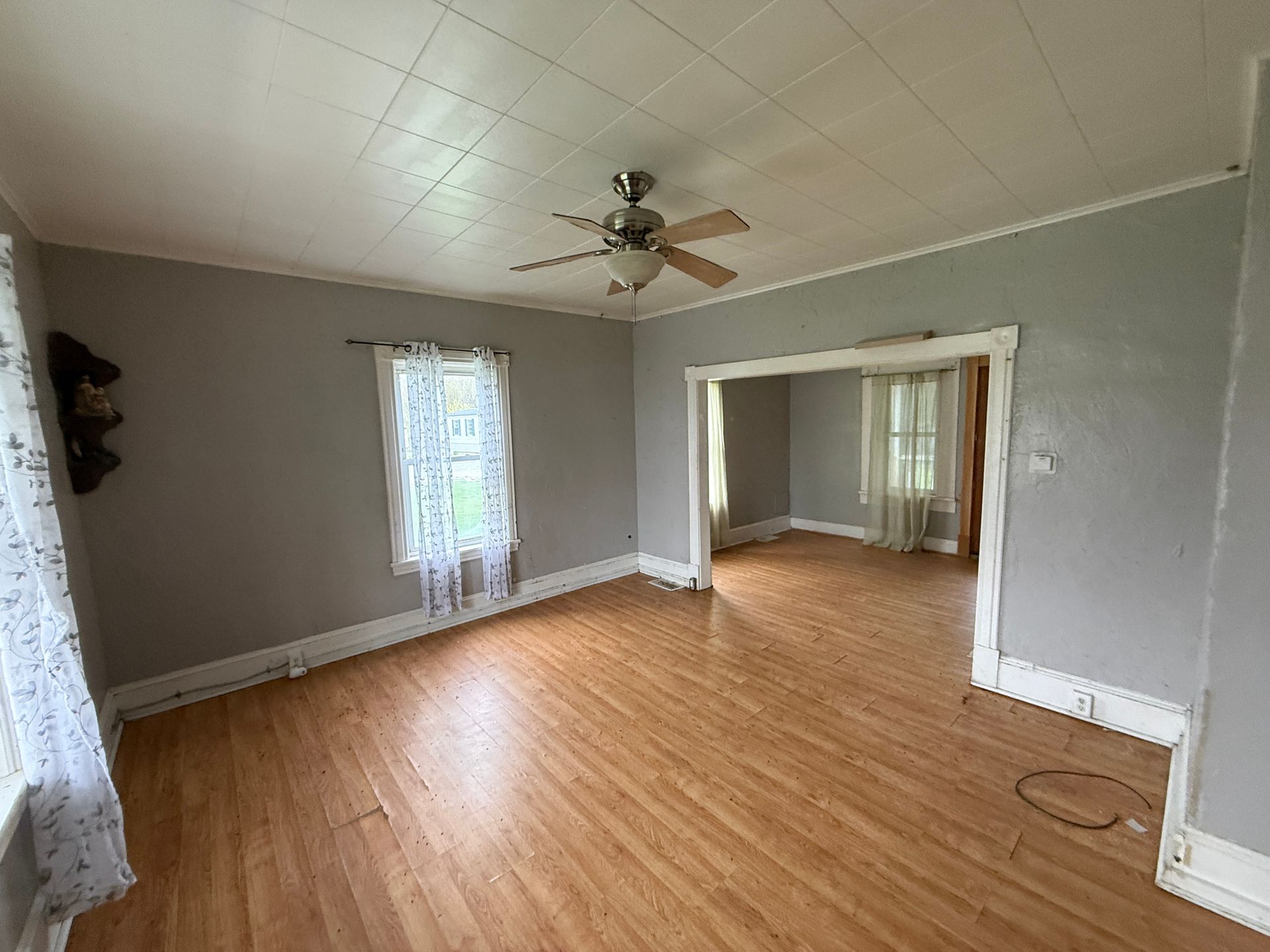 Empty living room with wood floors, gray walls, ceiling fan, and open doorway to another room