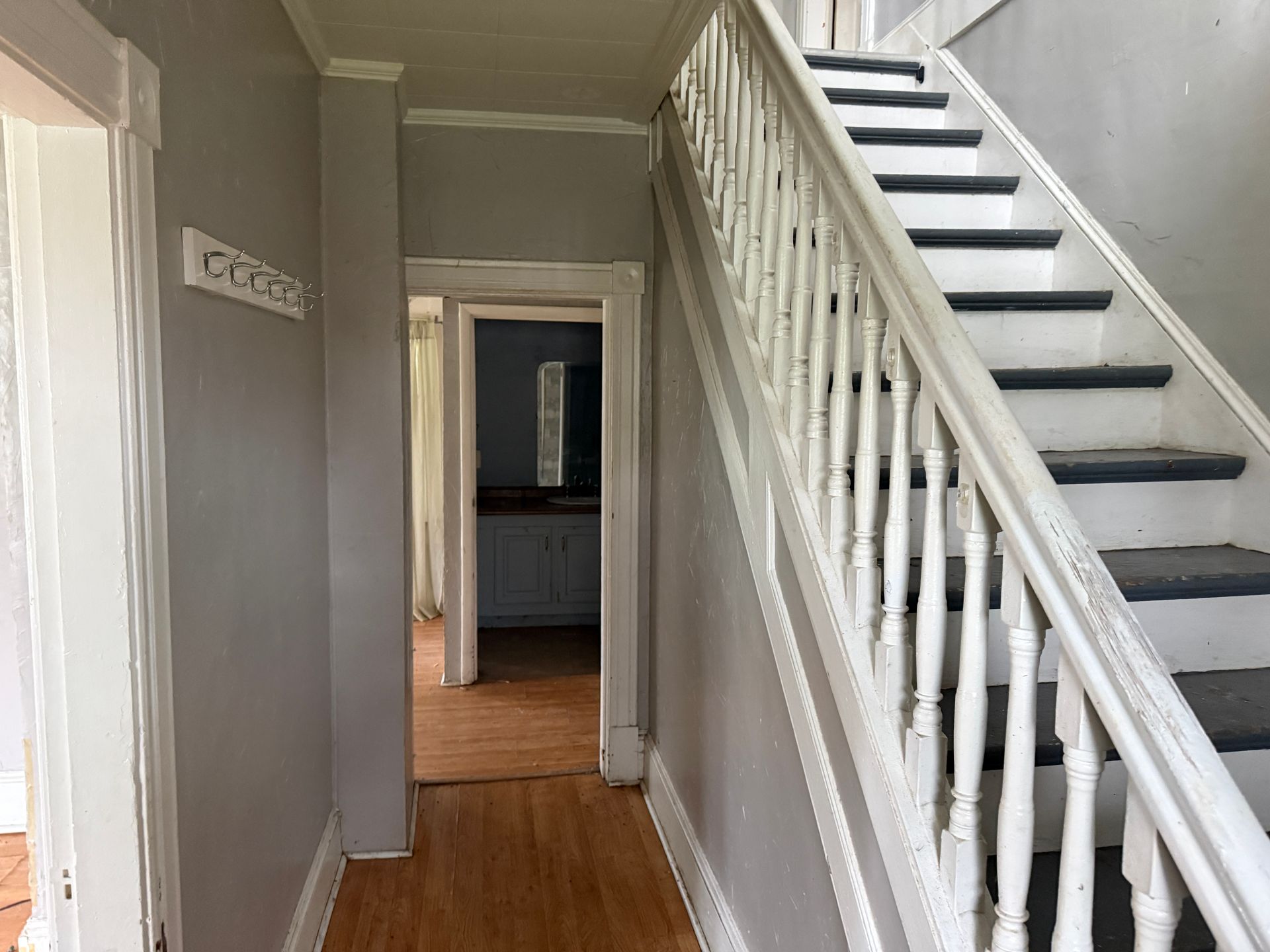 Interior hallway with wooden floor, staircase, and open doorway leading to a room