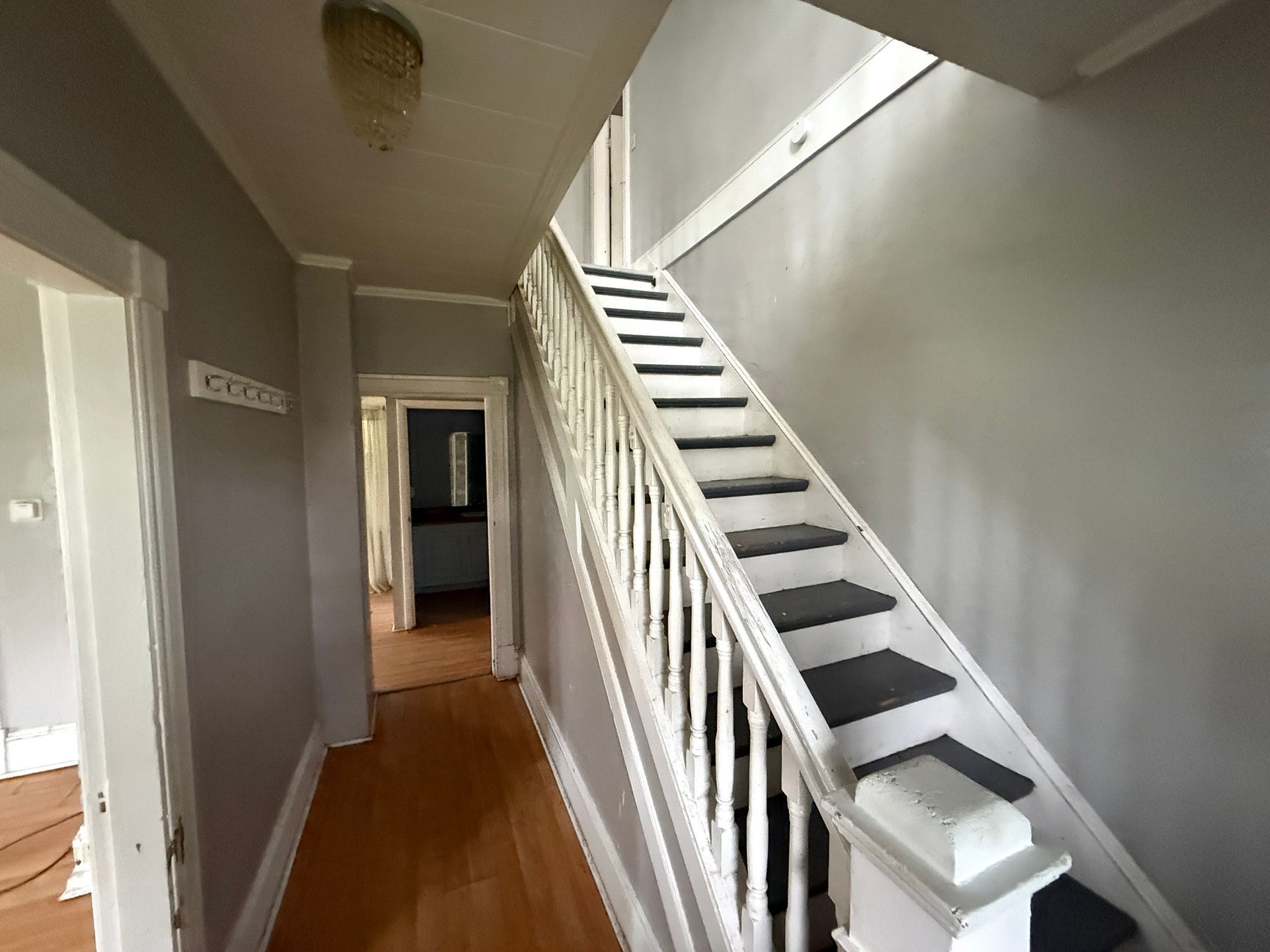 Narrow hallway with wooden floor and white staircase leading upward beside gray walls.