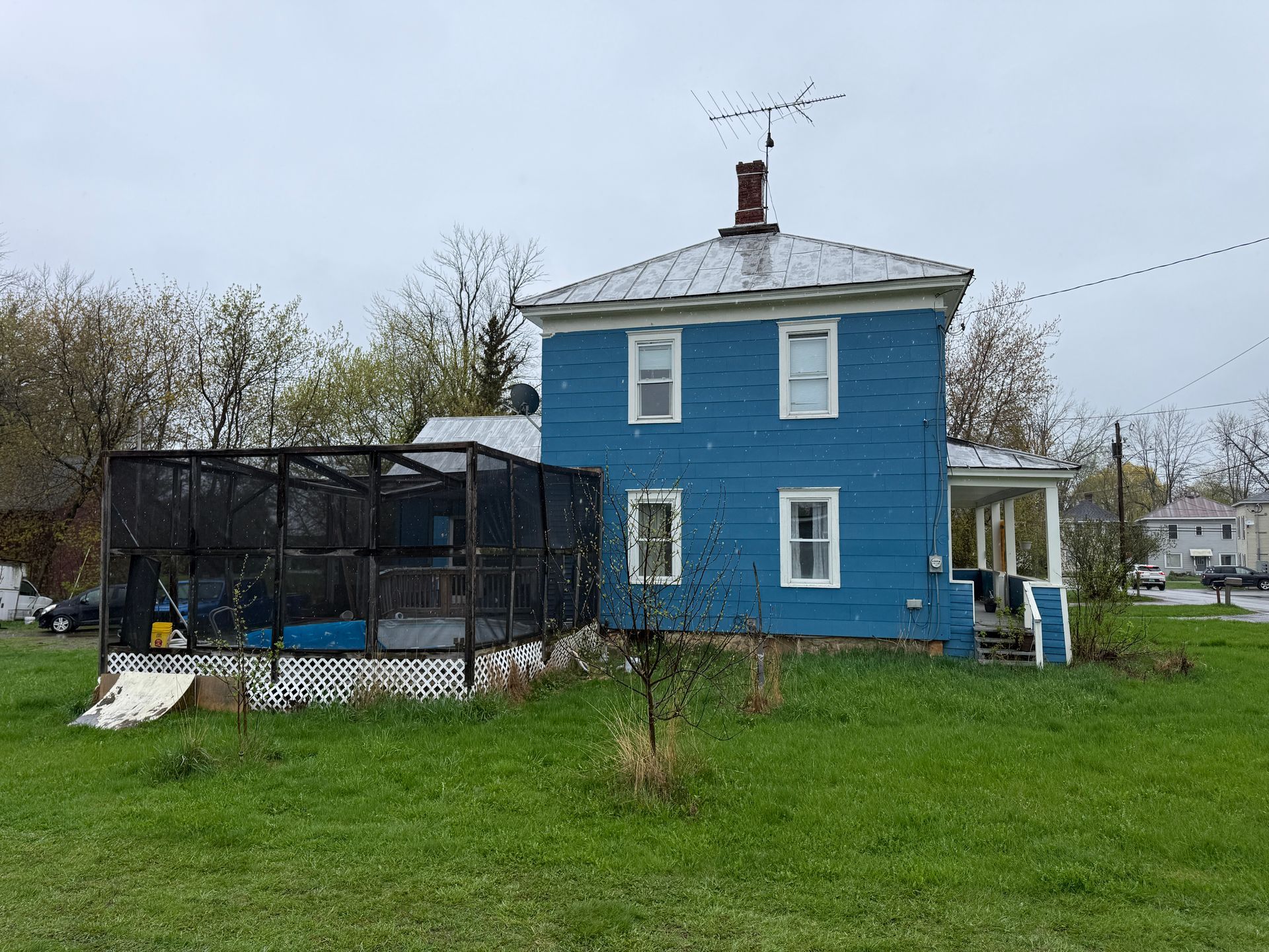 Blue two-story house with a fenced backyard and grassy lawn under an overcast sky