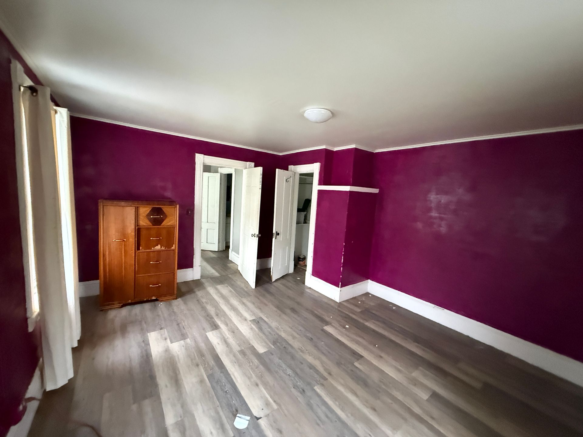 Empty room with purple walls, wood-look floor, and a small cabinet near a doorway.